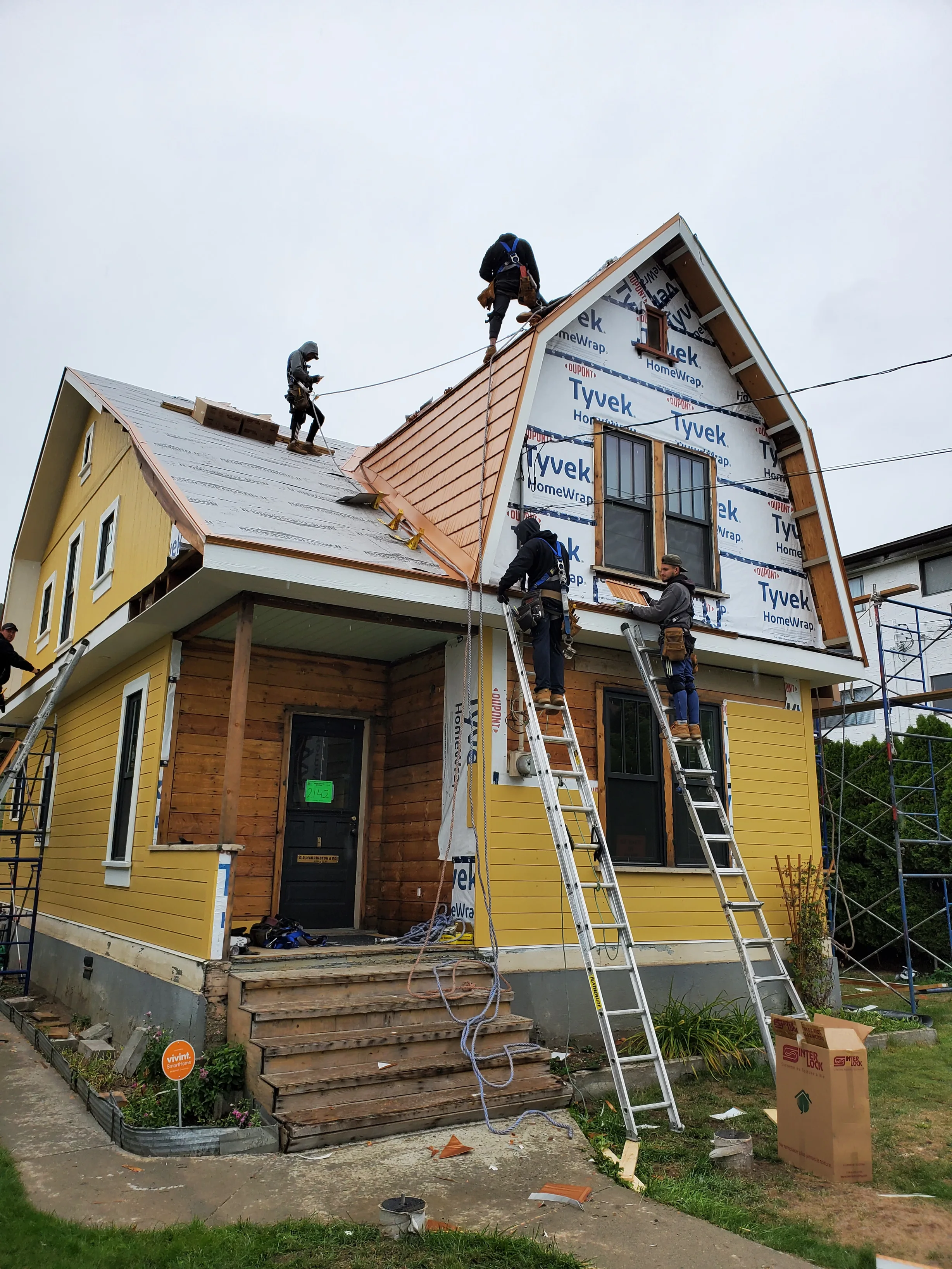 Copper Penny Interlock Cedar Shingle aluminum roof being installed on a yellow house with a metal roof under construction in a, Lumby, British Columbia