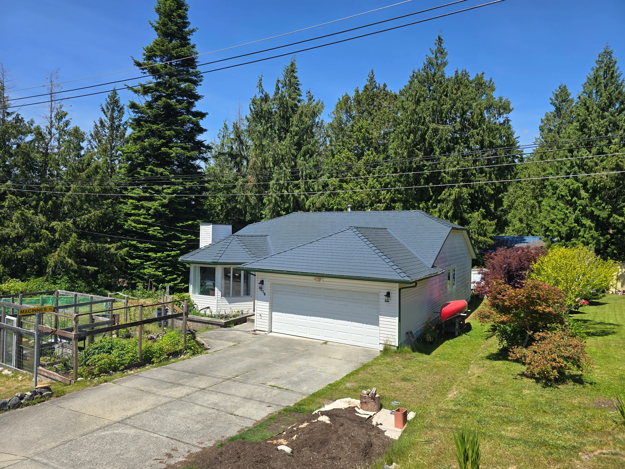 Deep Charcoal Interlock Slate aluminum roof on a white home with a metal roof among tall evergreens, Gibsons, British Columbia