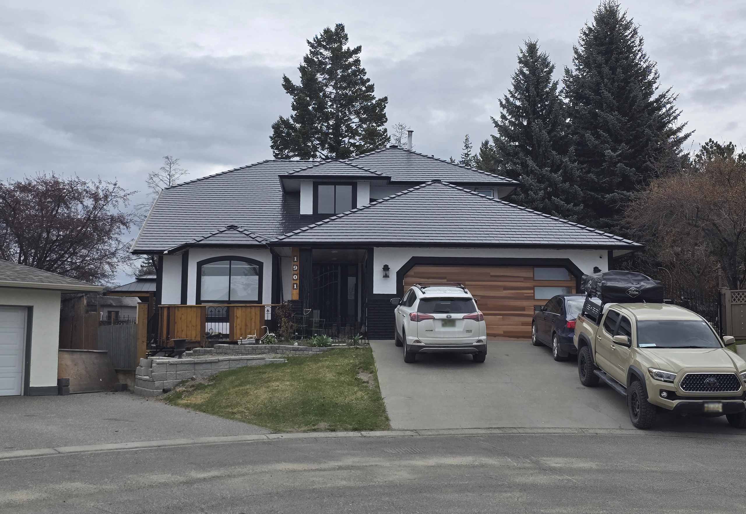 Modern single-family home in Kamloops BC with a complex multi-hip Interlock black aluminum slate roof featuring deep overhangs and cedar-accented garage.