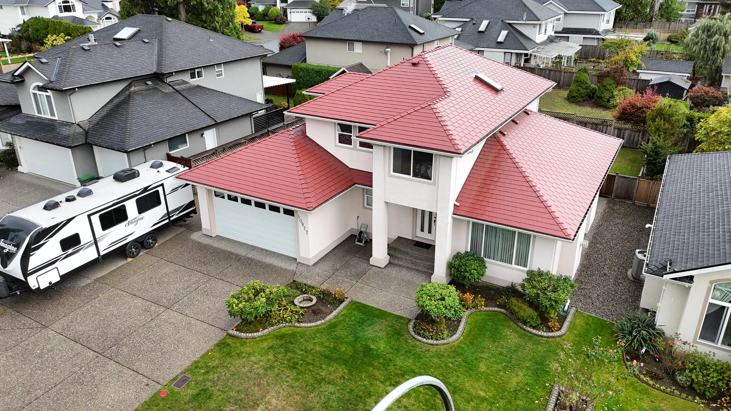 Tile Red Interlock Shingle aluminum roof on a white two-storey home with red roof among greenery, Surrey, British Columbia