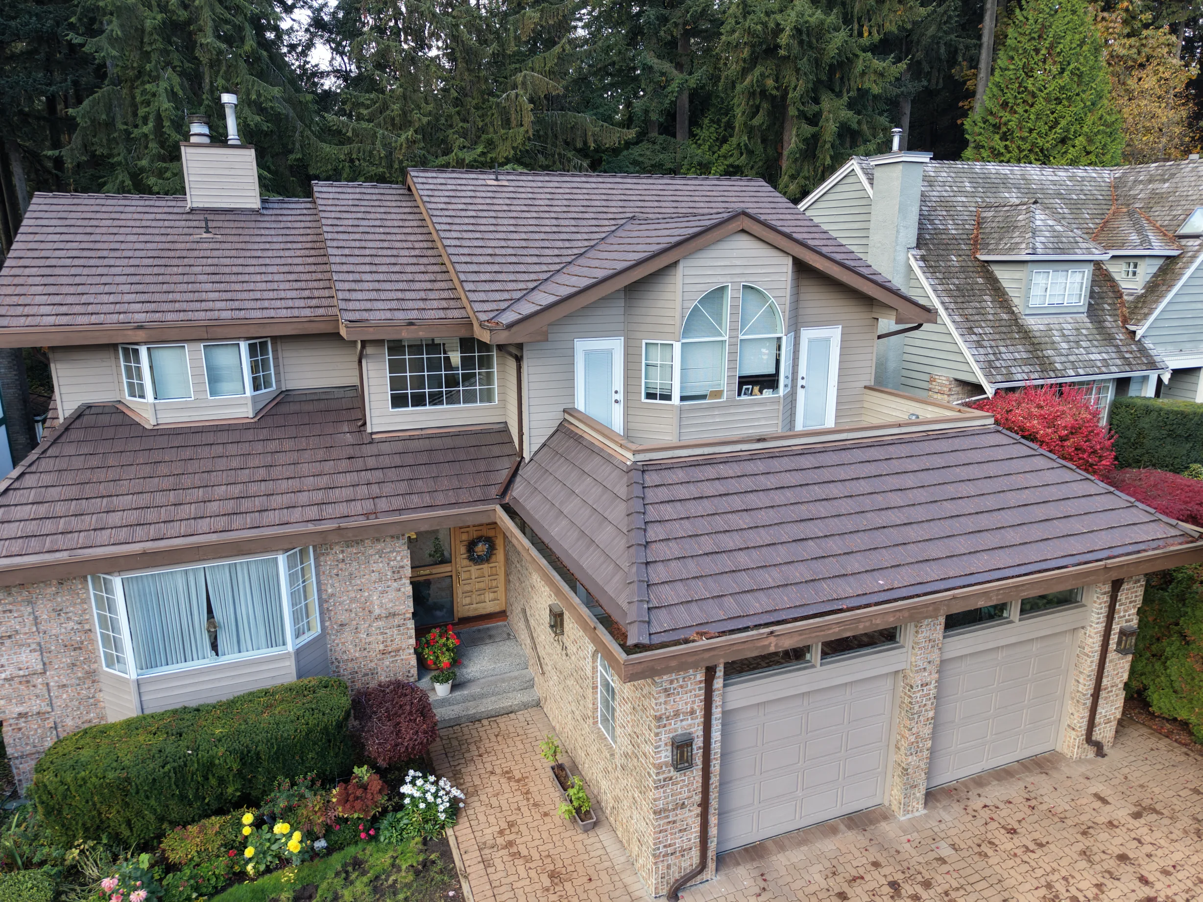 Colonial Brown Interlock Shake aluminum roof on a beige two-storey home with a dormer among tall trees, North Vancouver, British Columbia