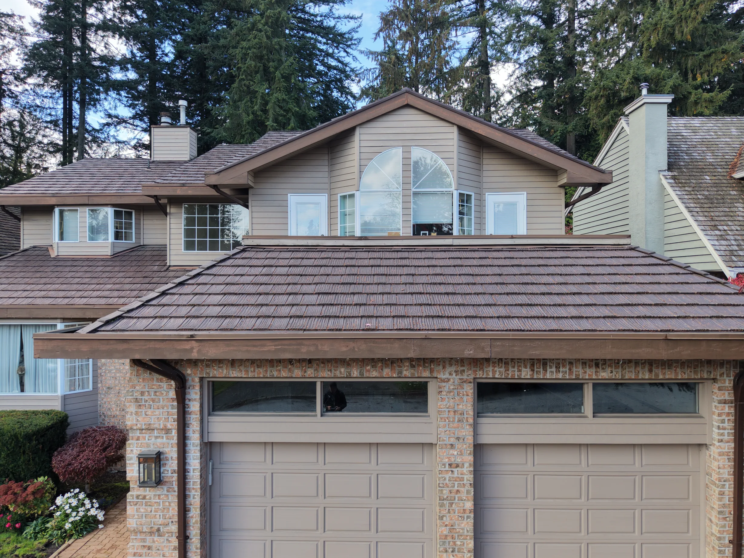 Colonial Brown Interlock Shake aluminum roof on a tan two-storey home with dormers in a forested urban area, North Vancouver, British Columbia