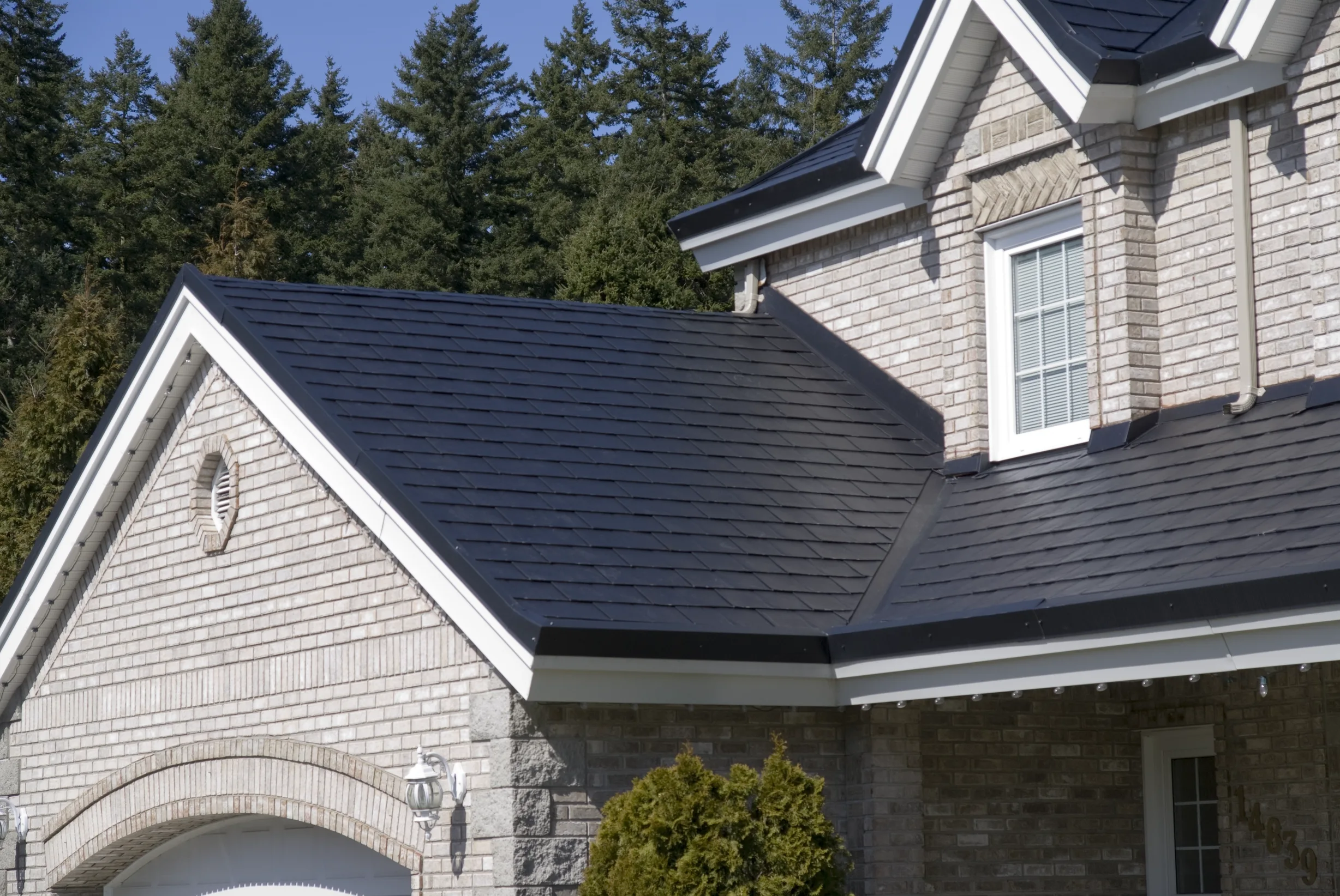 Black Interlock Slate aluminum roof on a grey two-storey Craftsman home with dormers among tall, Surrey, British Columbia