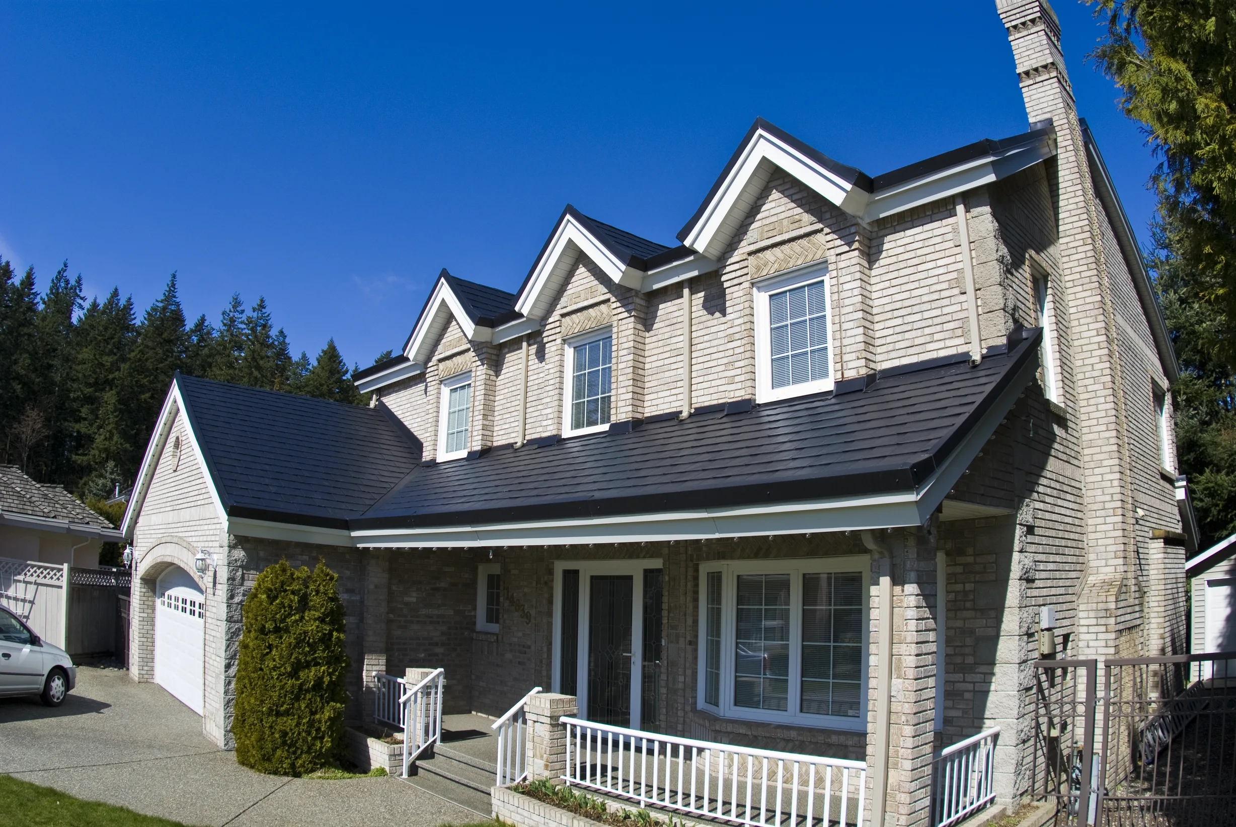 Black Interlock Slate aluminum roof on a beige two-storey Colonial home with a dormer among tall, Surrey, British Columbia