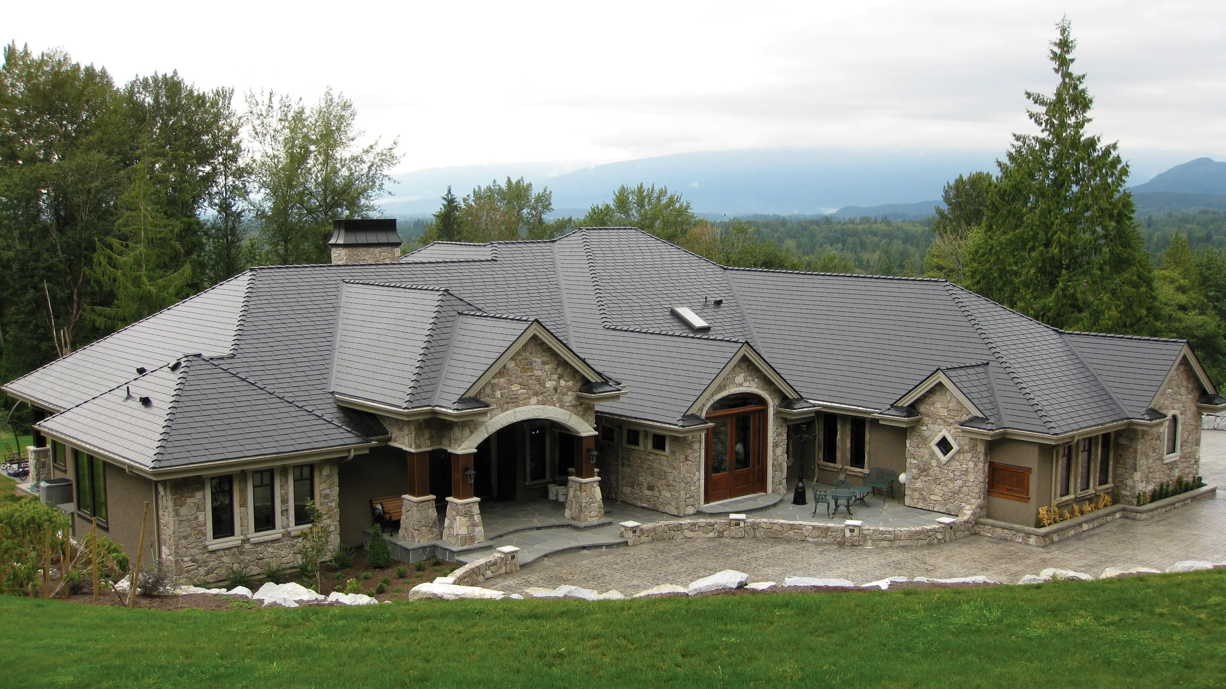 Charcoal Grey Interlock Slate aluminum roof on a stone ranch home with a metal roof in a forested mountain, Mission, British Columbia