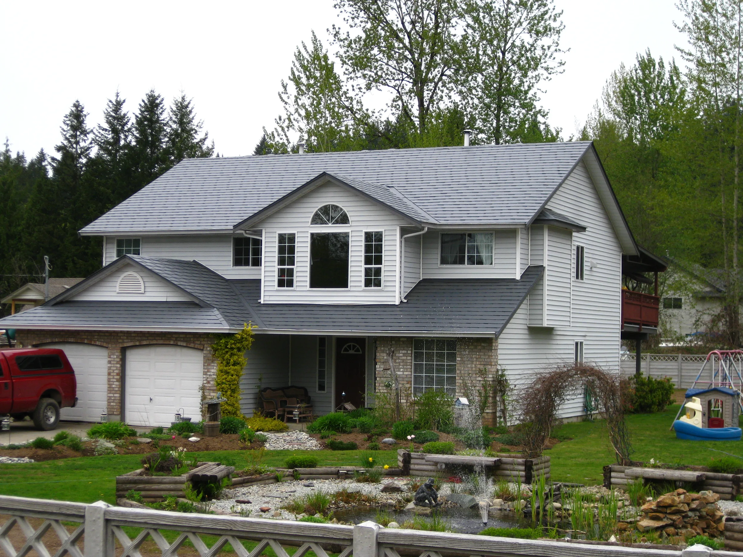Charcoal Grey Interlock Slate aluminum roof on a white two-storey home with a metal roof among tall trees, Mission, British Columbia