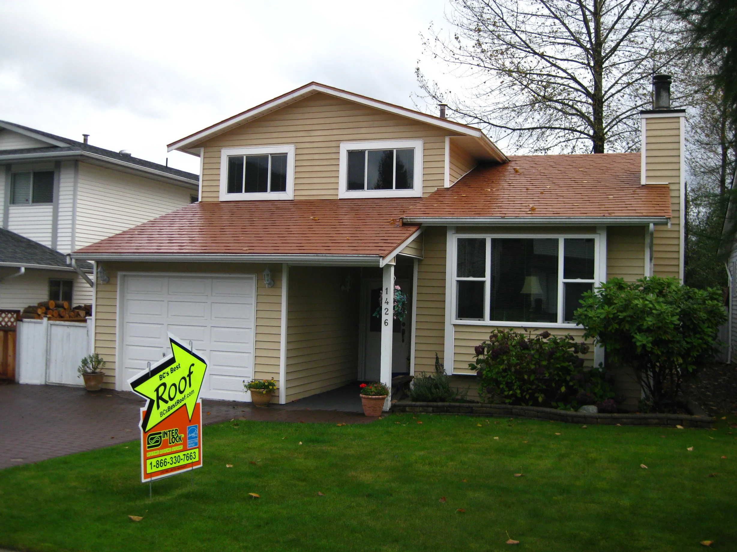 Aged Copper Interlock Slate aluminum roof on a yellow two-storey home with dormers among tall pines, Coquitlam, British Columbia