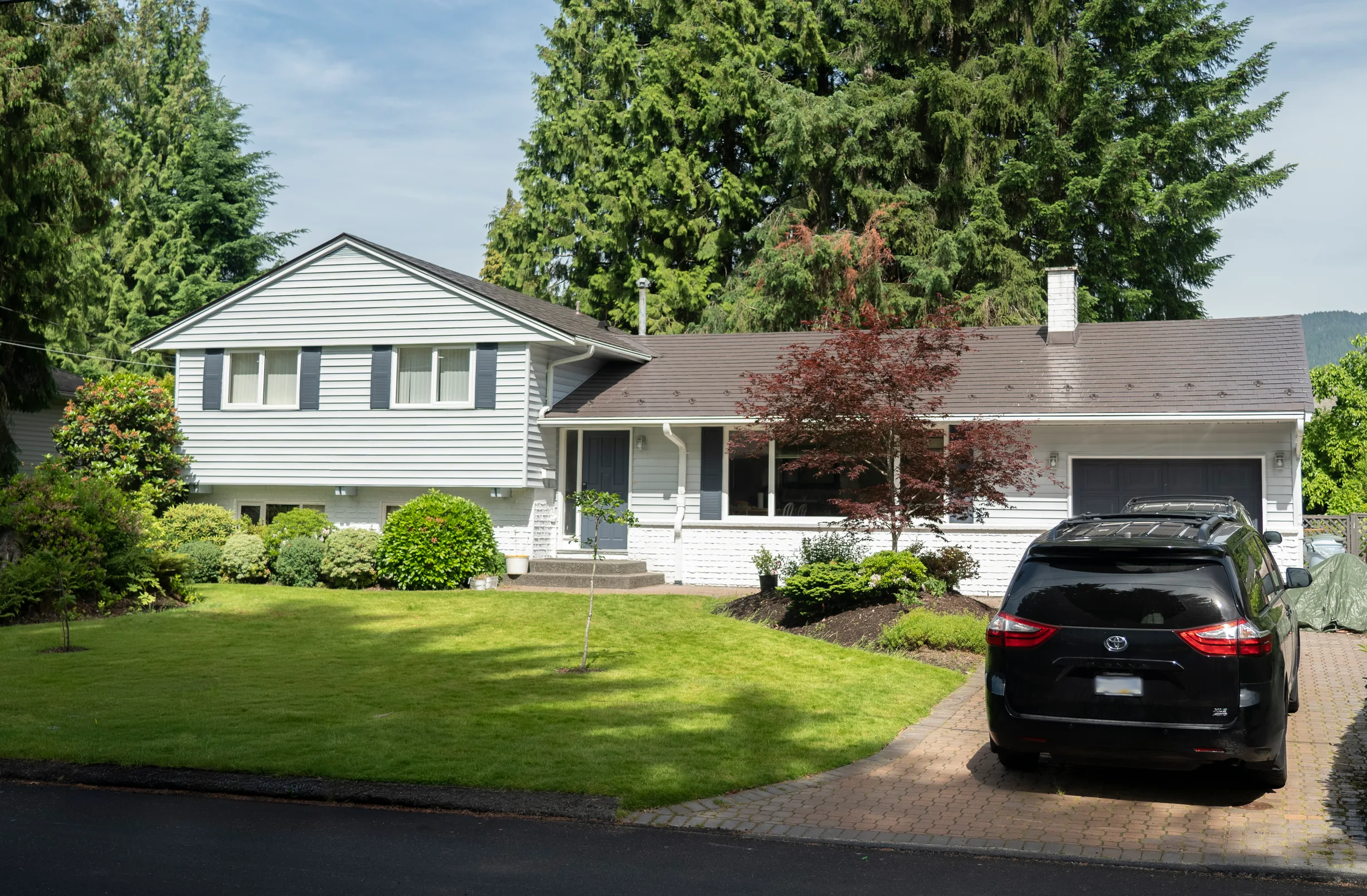 Weathered Interlock Slate aluminum roof on a white ranch home with a metal roof among tall trees, Burnaby, British Columbia