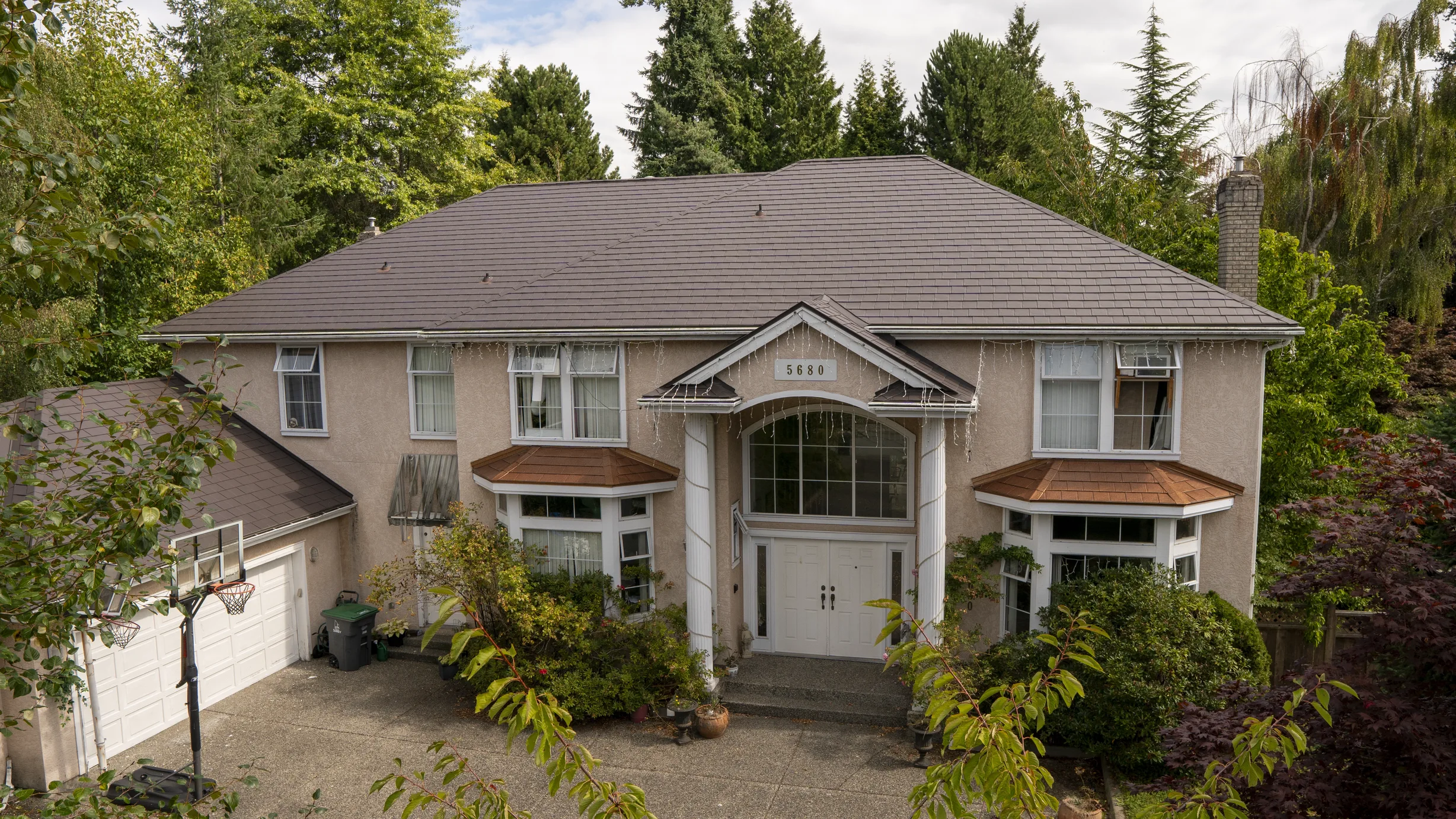 Tudor Brown Interlock Slate aluminum roof on a two-storey Tudor home with dormers among tall trees, Surrey, British Columbia
