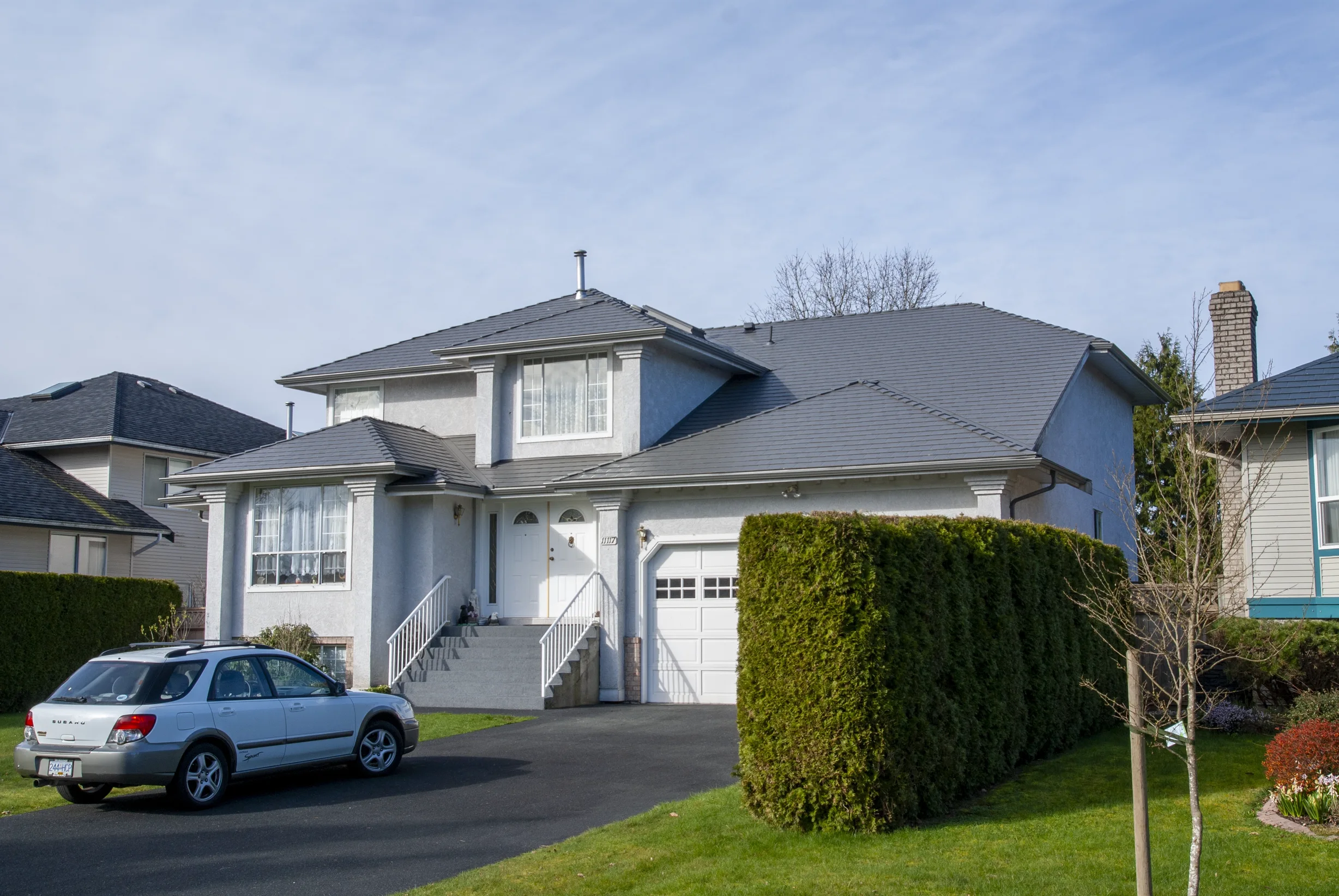 Musket Grey Interlock Slate aluminum roof on a two-storey home with a grey metal roof in a lush green, Surrey, British Columbia