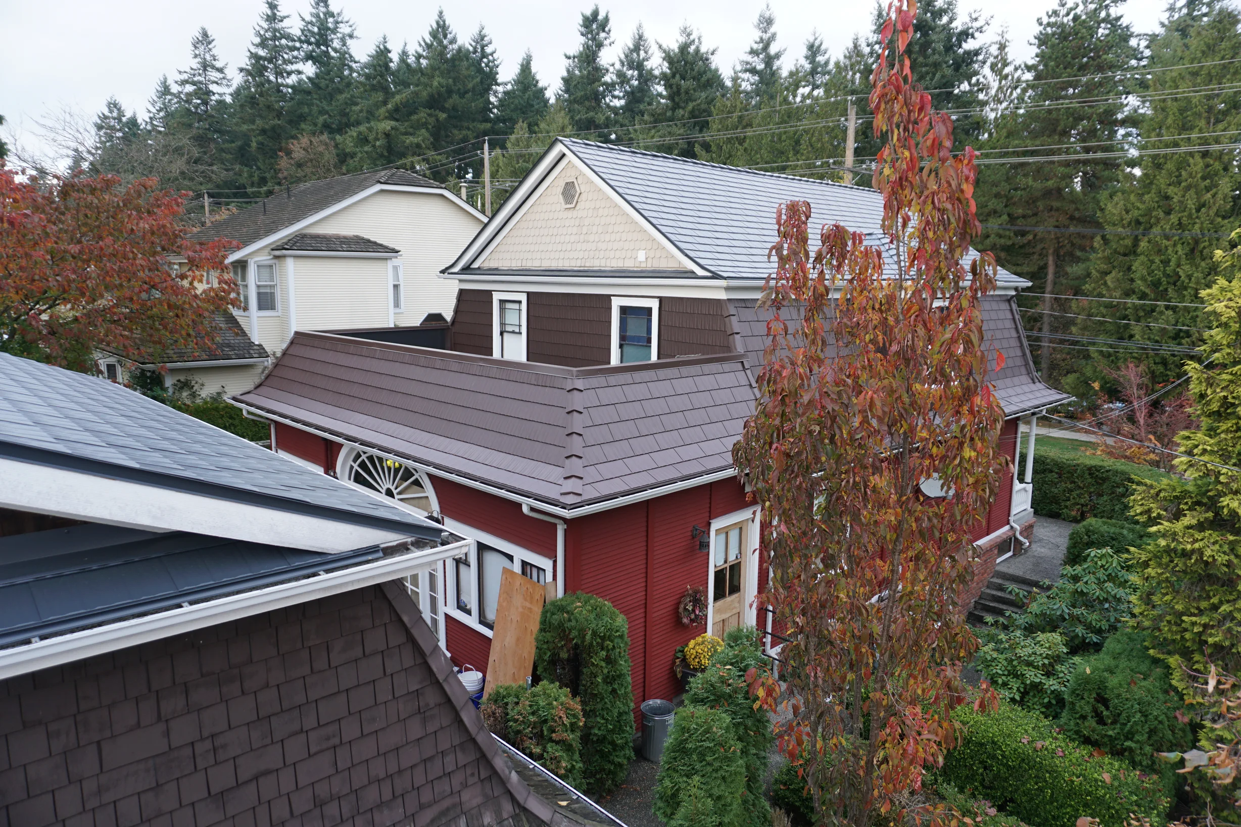Colonial Brown Interlock Cedar Shingle aluminum roof on a red two-storey home with dormers among tall pines, New Westminster, British Columbia