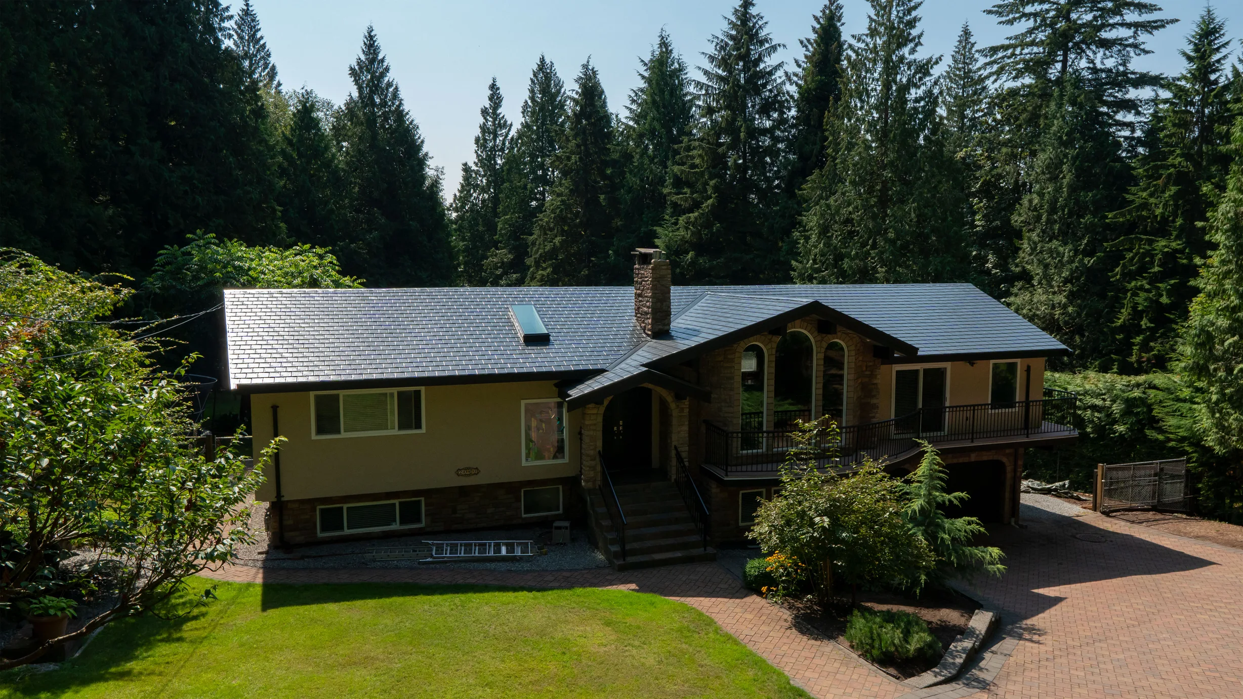 Deep Charcoal Interlock Slate aluminum roof on a brown two-storey home with dormers among tall pines, Anmore, British Columbia