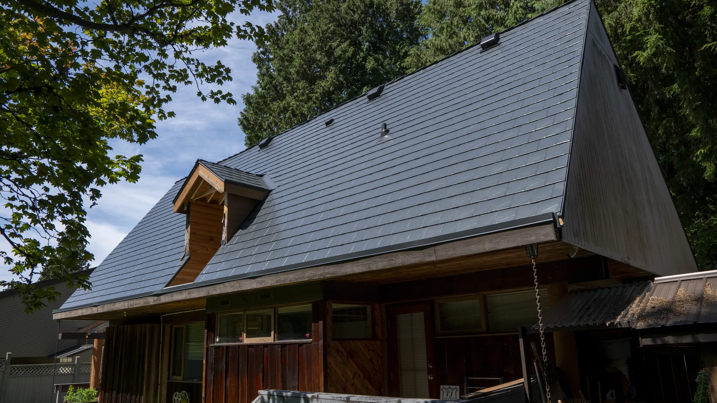 Deep Charcoal Interlock Slate aluminum roof on a brown A-frame home with a metal roof among tall trees, Burnaby, British Columbia