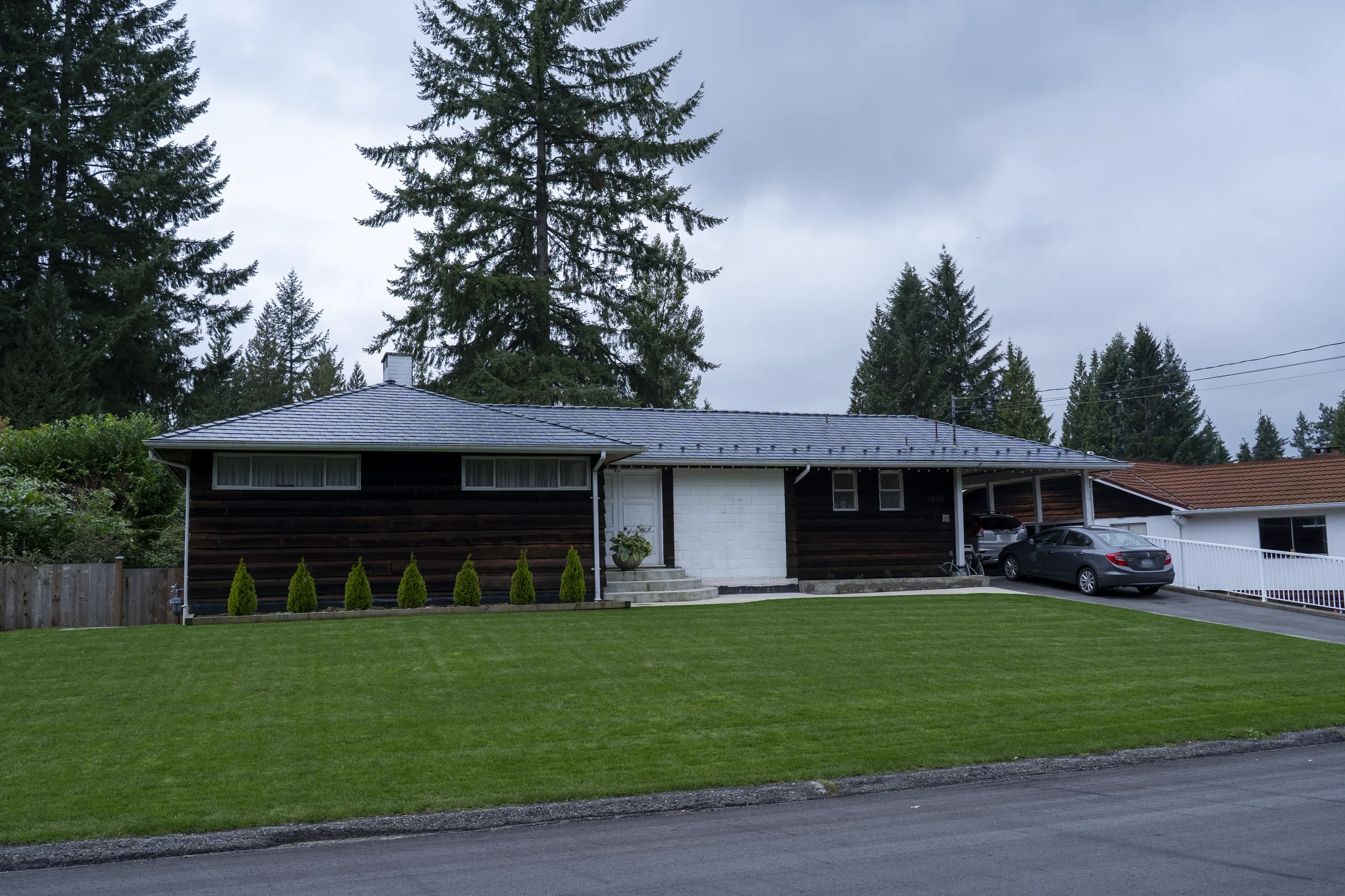 Deep Charcoal Interlock Slate aluminum roof on a brown ranch style home with a metal roof among tall trees, North Vancouver, British Columbia