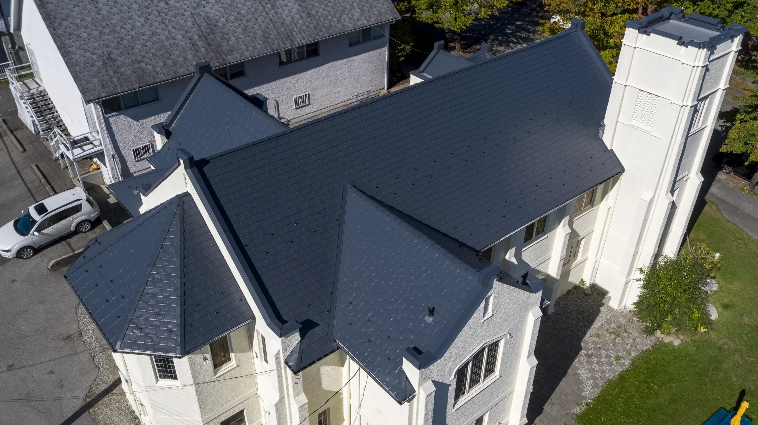 Deep Charcoal Interlock Slate aluminum roof on a white single-family home with a metal roof and tall trees, Vancouver, British Columbia