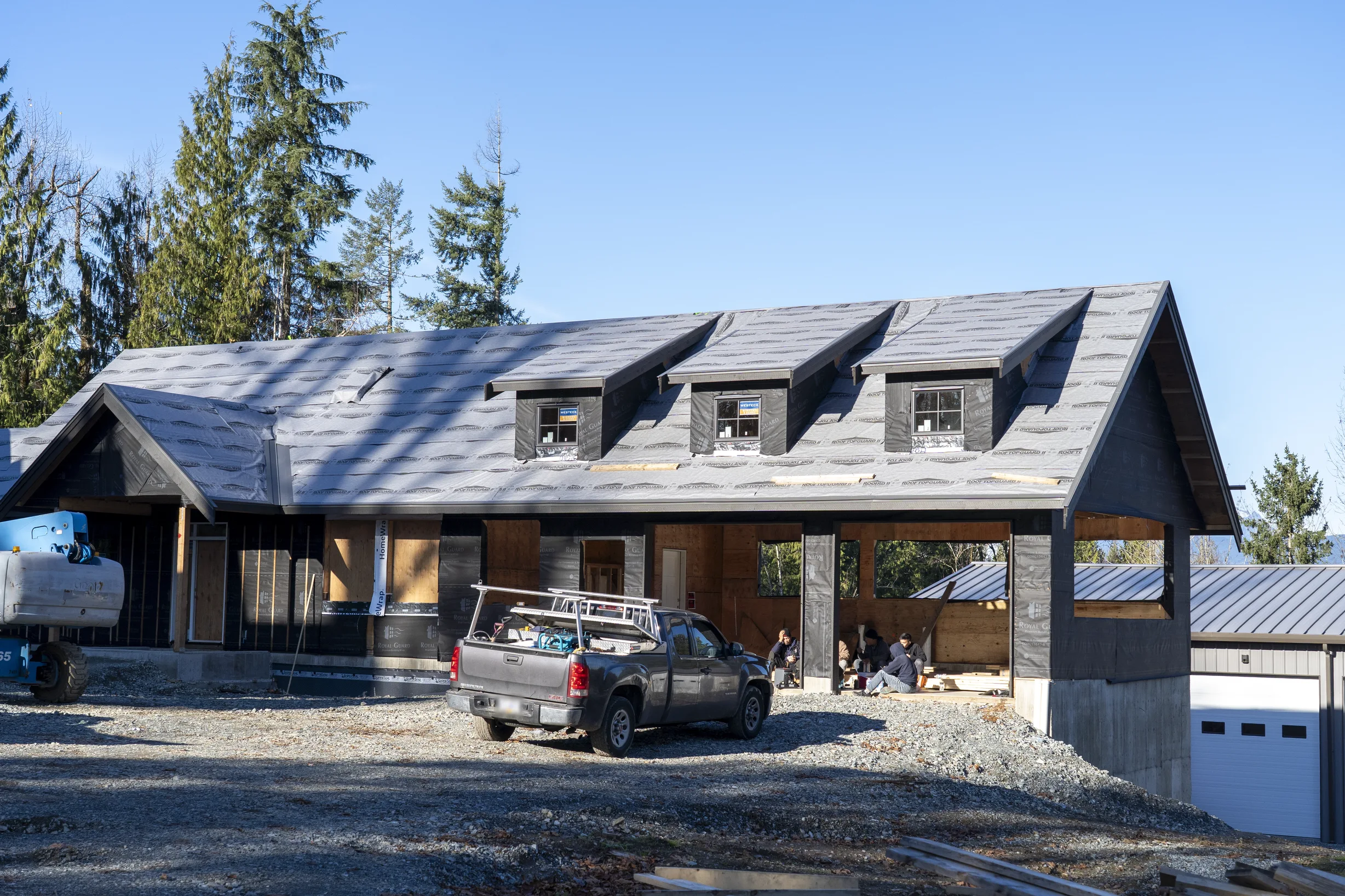 Musket Grey Interlock Slate aluminum roof being installed on a metal roof on a single-storey rural home among tall pines, Abbotsford, British Columbia