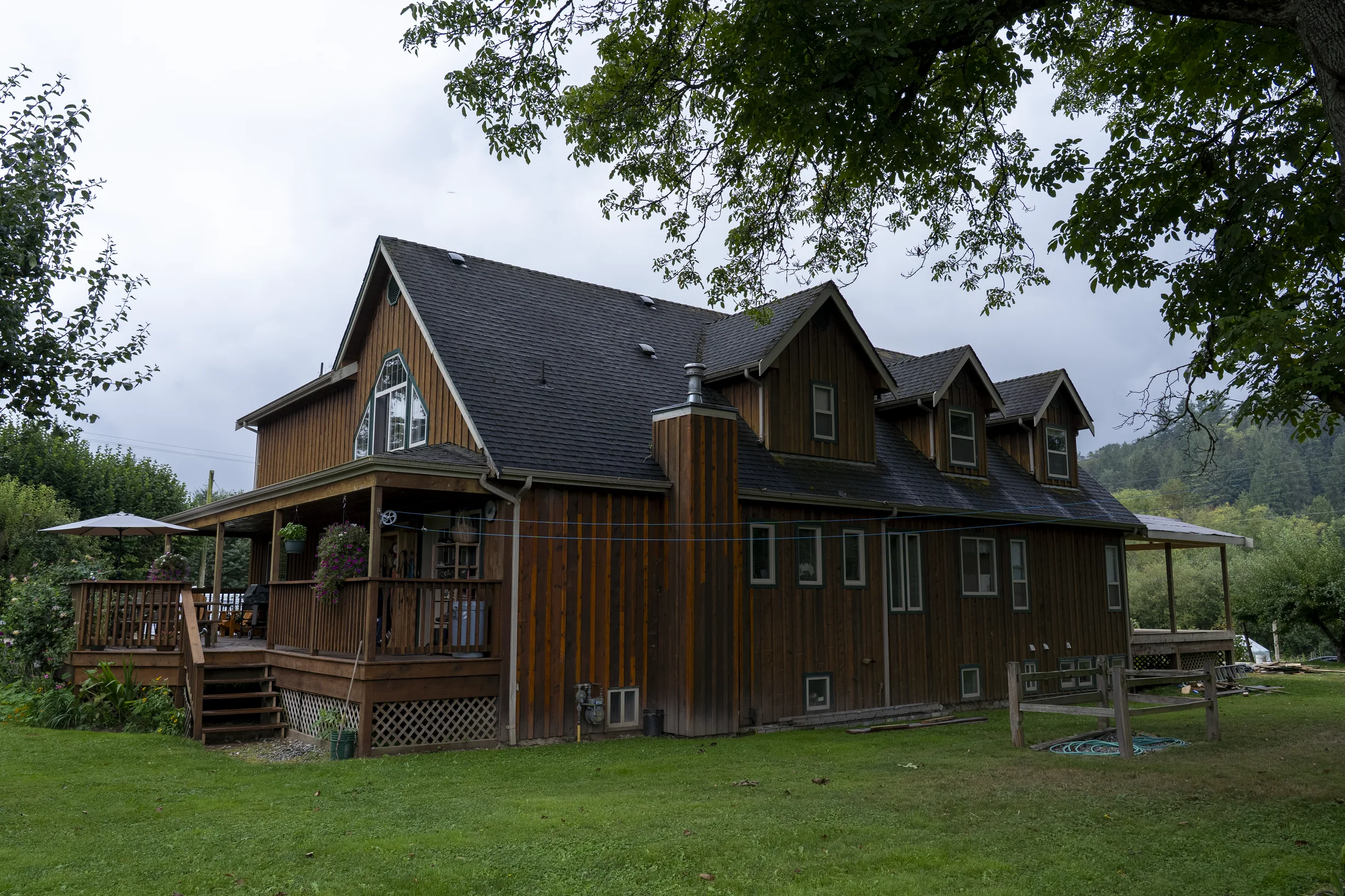 Hunter Green Interlock Slate aluminum roof being installed on a brown home with dormer and chimney among tall trees, Langley, British Columbia