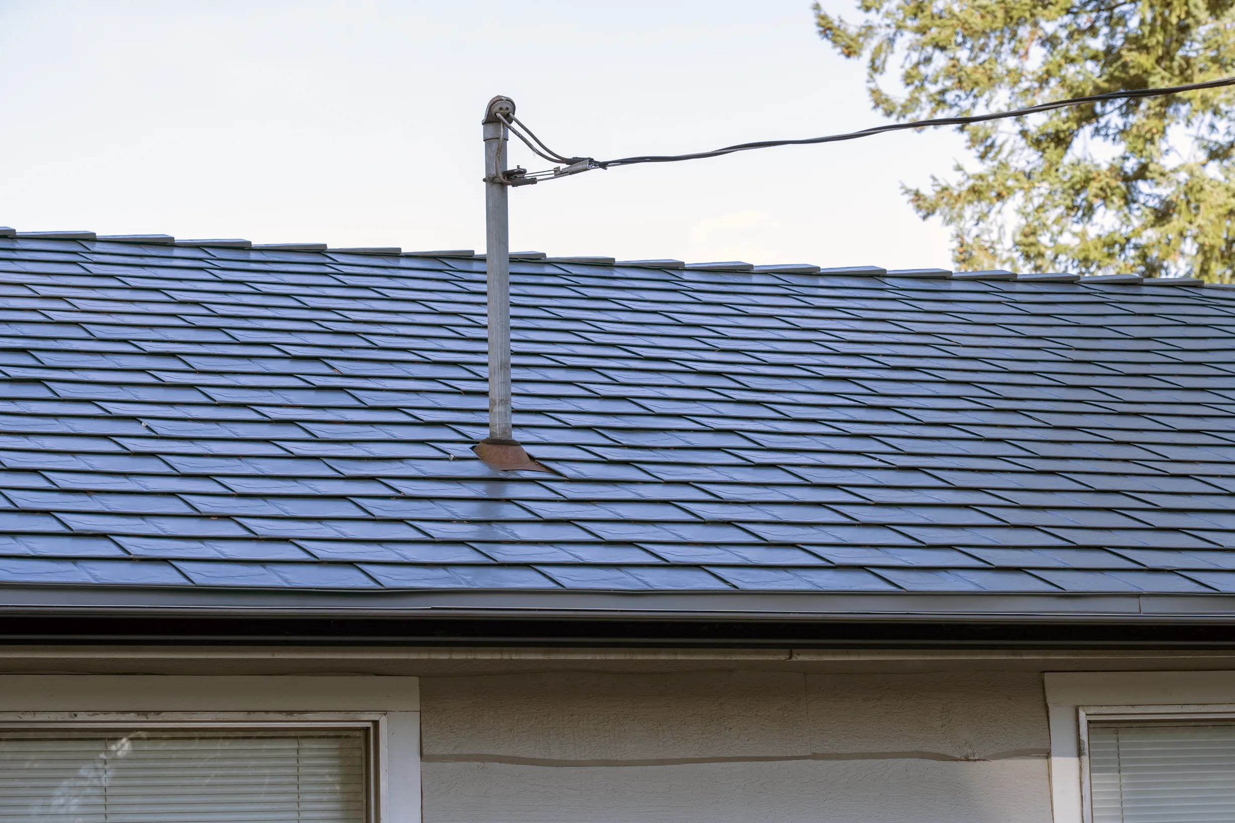 Deep Charcoal Interlock Slate aluminum roof on a beige single-family home with a metal roof in a forested, Mission, British Columbia