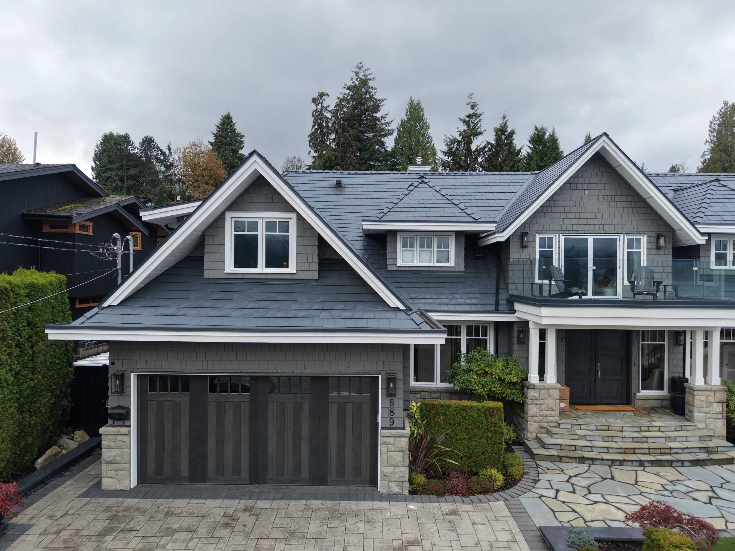 Deep Charcoal Interlock Slate aluminum roof on a grey two-storey home with dormers among tall pines, North Vancouver, British Columbia