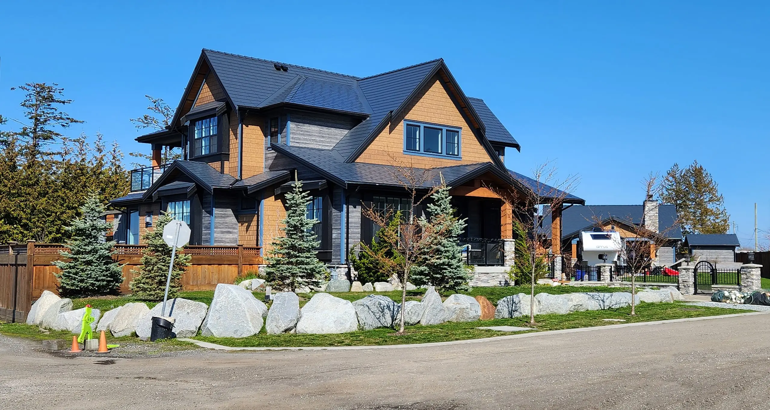 Two-storey Craftsman home in Tsawwassen BC with a complex steep Interlock aluminum slate roof in deep charcoal, boulder-lined landscaping, and cedar accents.