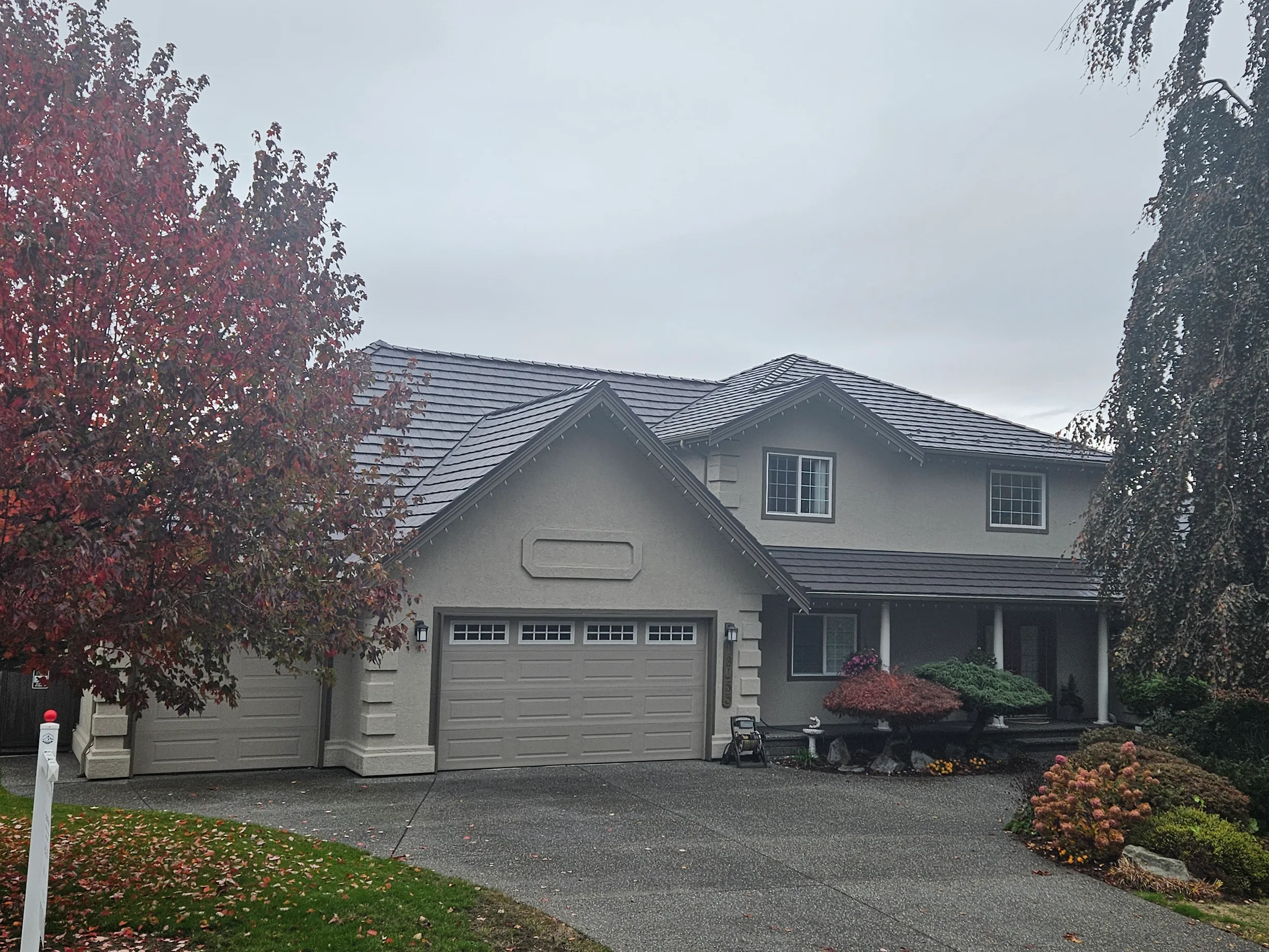 Tudor Brown Interlock Shake aluminum roof on a beige two-storey home with a gable and dormer in autumn, Surrey, British Columbia
