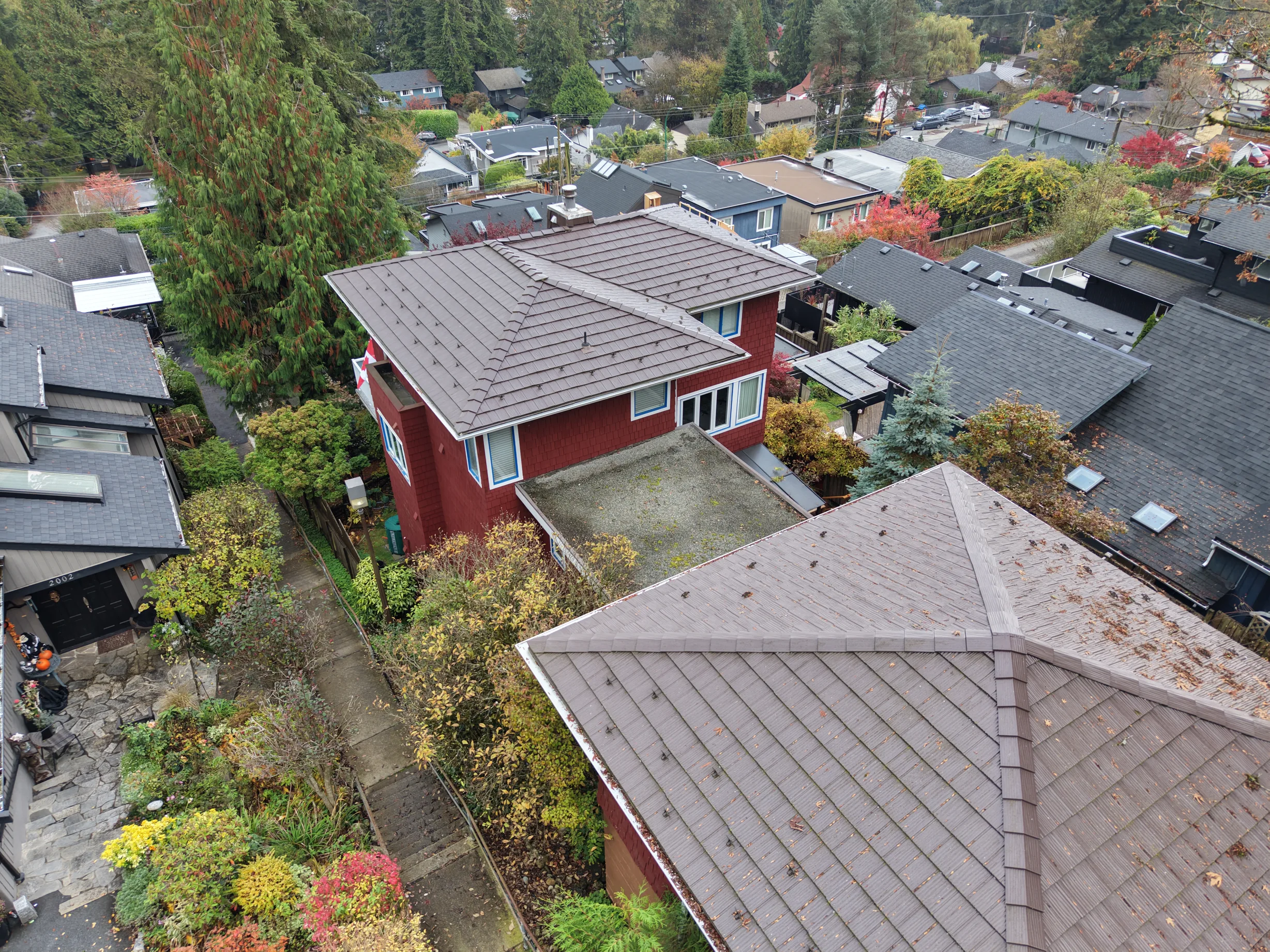 Colonial Brown Interlock Shake aluminum roof on a red Colonial two-storey home with dormers among tall, North Vancouver, British Columbia
