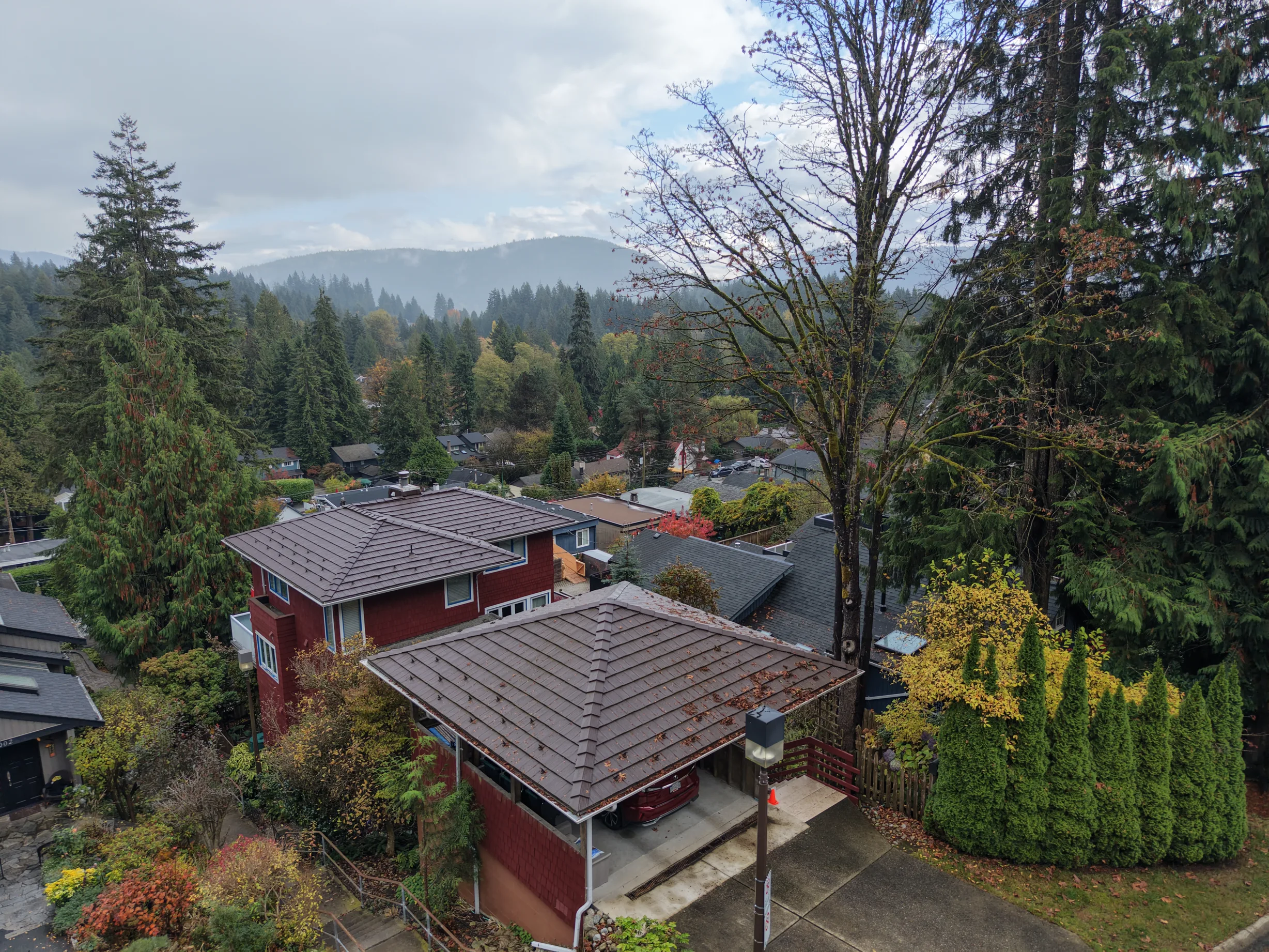 Colonial Brown Interlock Shake aluminum roof on a red two-storey home with a brown metal roof among tall, North Vancouver, British Columbia