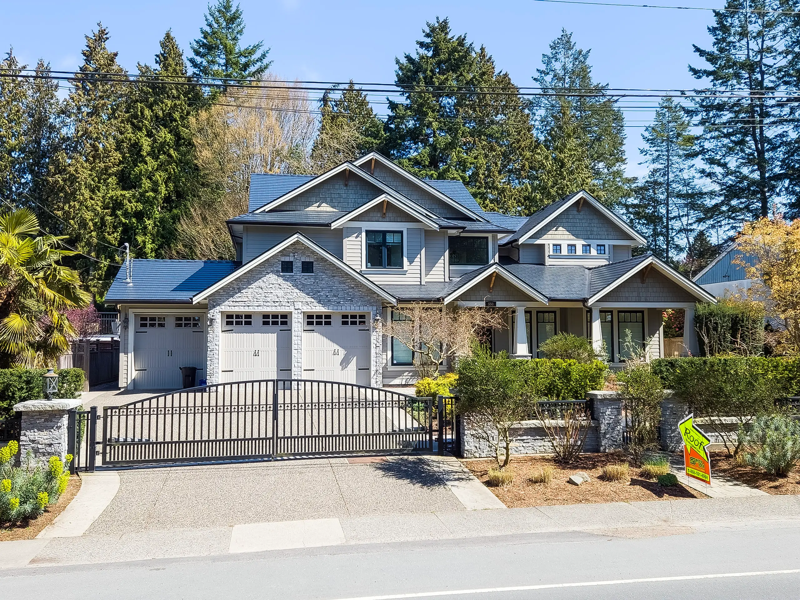 Large Craftsman home in Tsawwassen BC with dark black Interlock cedar-shingle metal roof featuring multiple gables, dormers, and stone accents behind iron gate.
