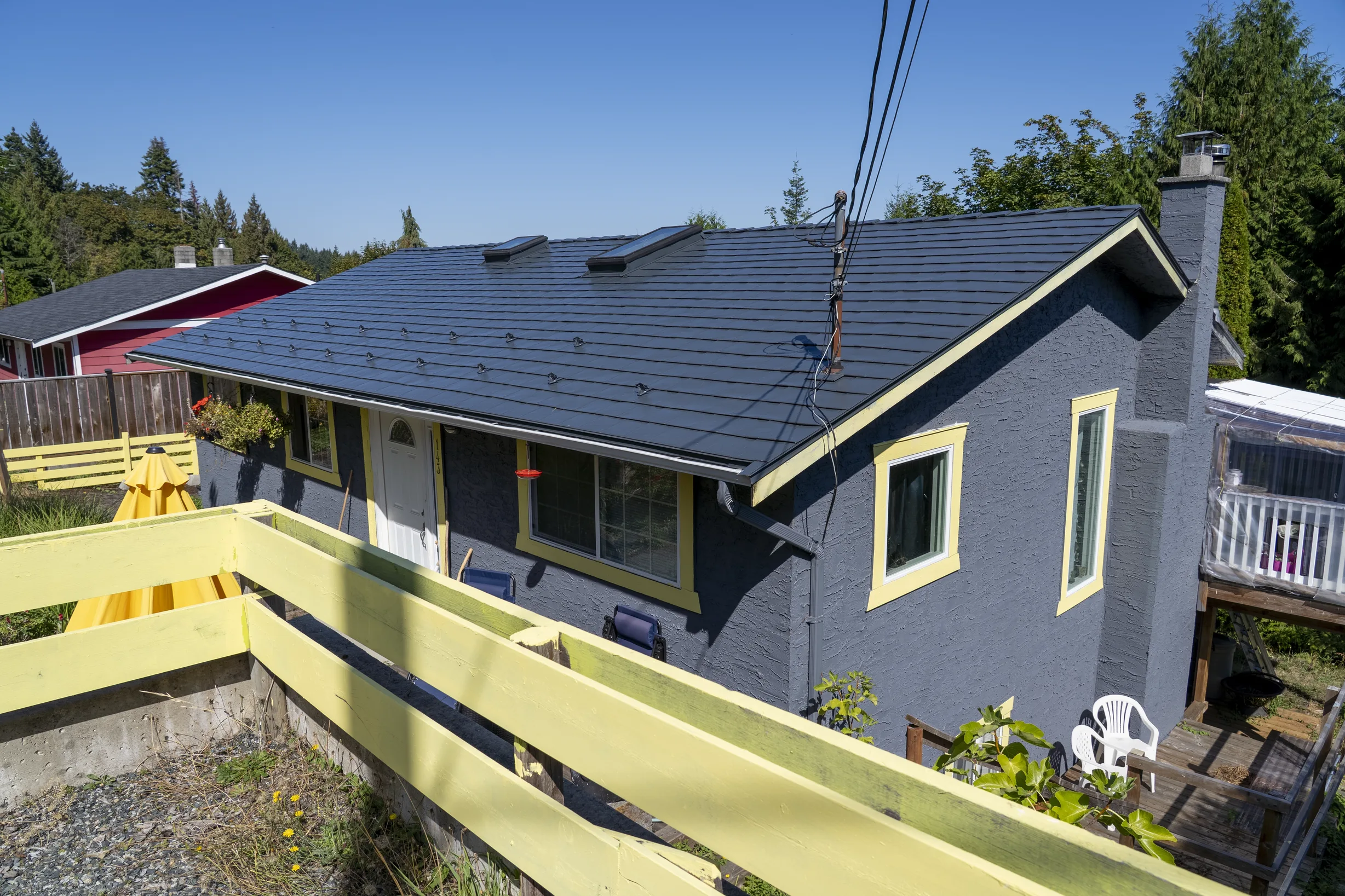 Deep Charcoal Interlock Slate aluminum roof on a two-storey home with a dark grey metal roof among tall, Ladysmith, British Columbia