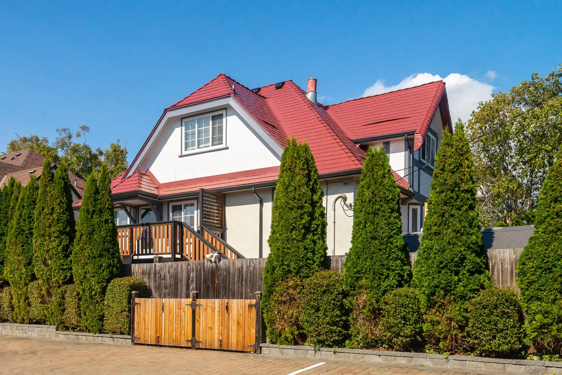 Two-storey Tudor-style home in Victoria BC featuring a complex multi-hip Interlock aluminum slate roof in tile red with dormer, chimney, and cedar privacy hedge.