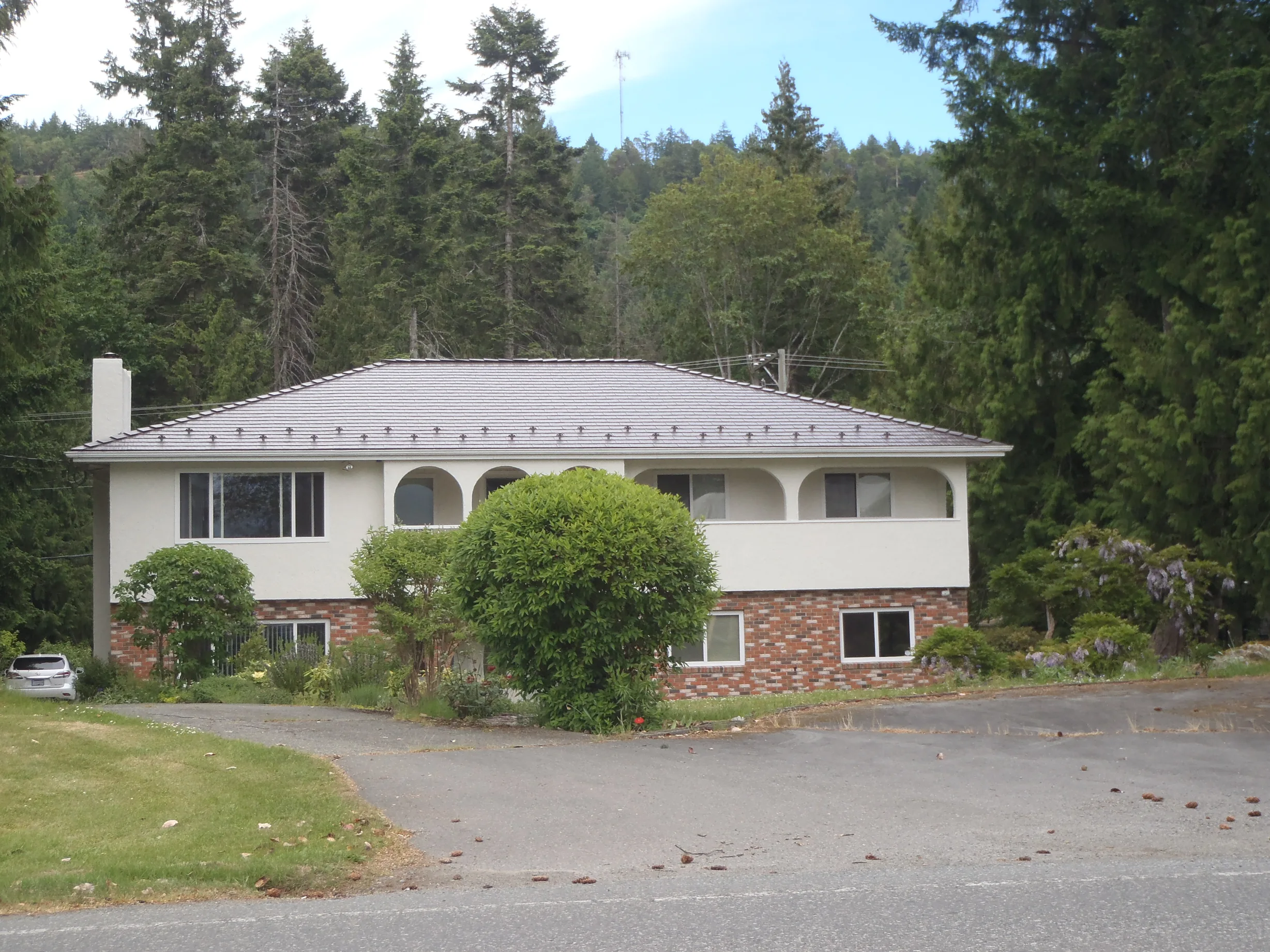 Tudor Brown Interlock Cedar Shingle aluminum roof on a Tudor style home with a brown metal roof among tall trees, Ladysmith, British Columbia