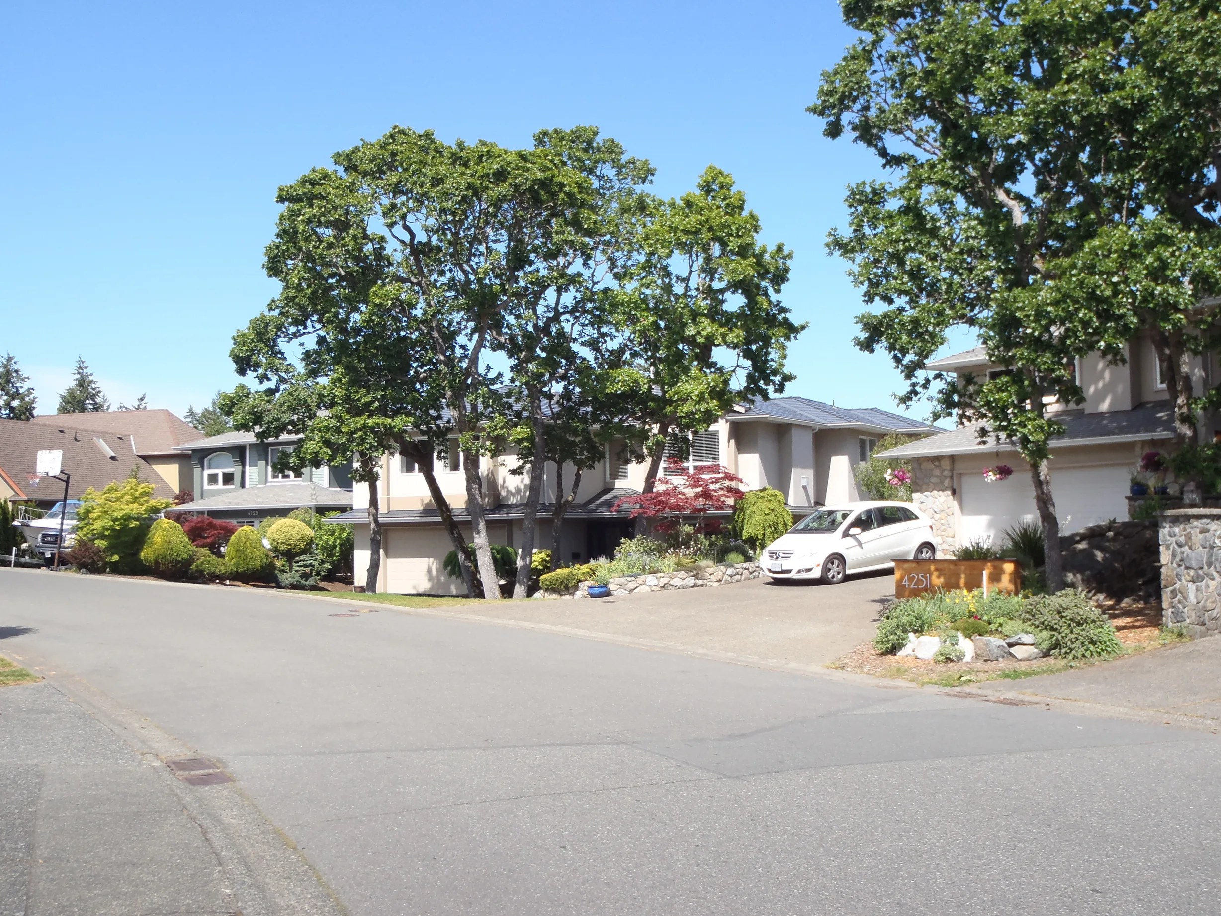 Deep Charcoal Interlock Slate aluminum roof on a beige two-storey home with a metal roof among tall pines, Victoria, British Columbia
