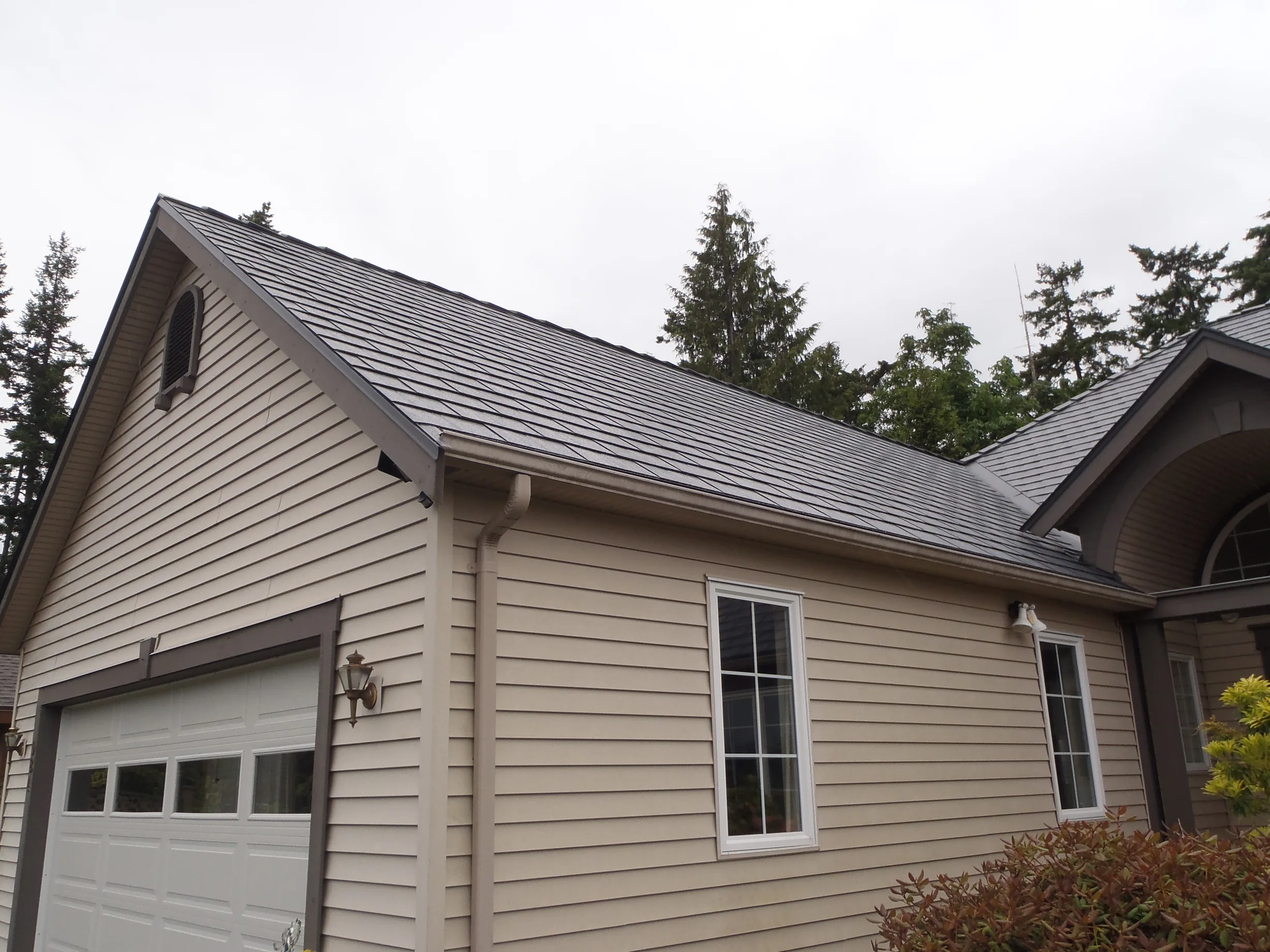 Deep Charcoal Interlock Slate aluminum roof on a tan single-family home with a gable roof among coastal, Qualicum Beach, British Columbia