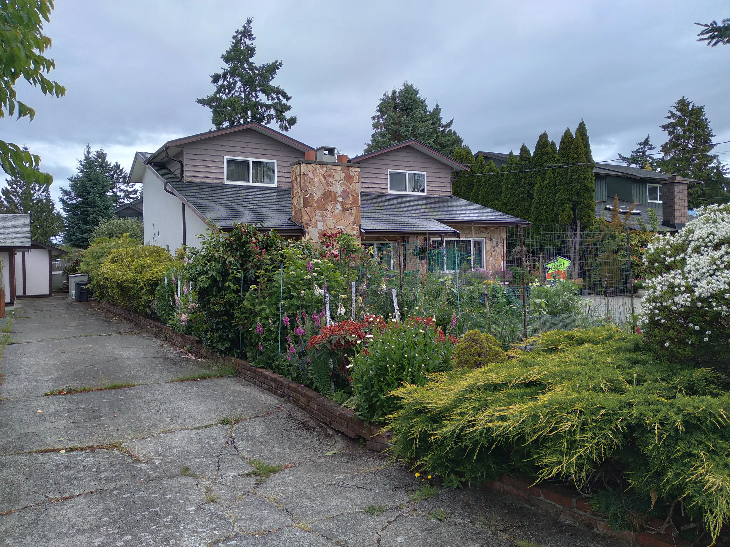 Black Interlock Slate aluminum roof on a two-storey home with a metal roof among trees and shrubs, Victoria, British Columbia