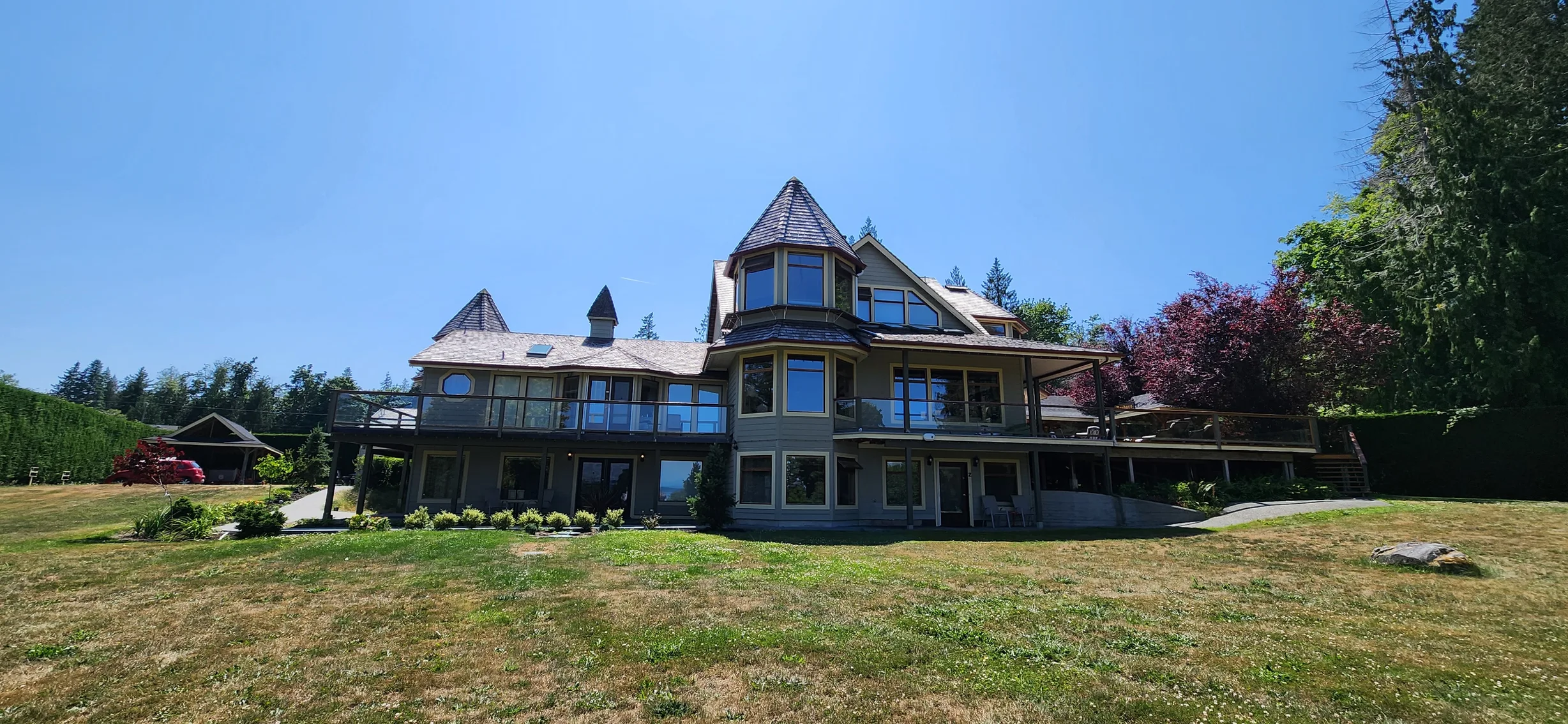 Copper Penny Interlock Slate aluminum roof on a brown two-storey home with dormers among tall pines, Ladysmith, British Columbia