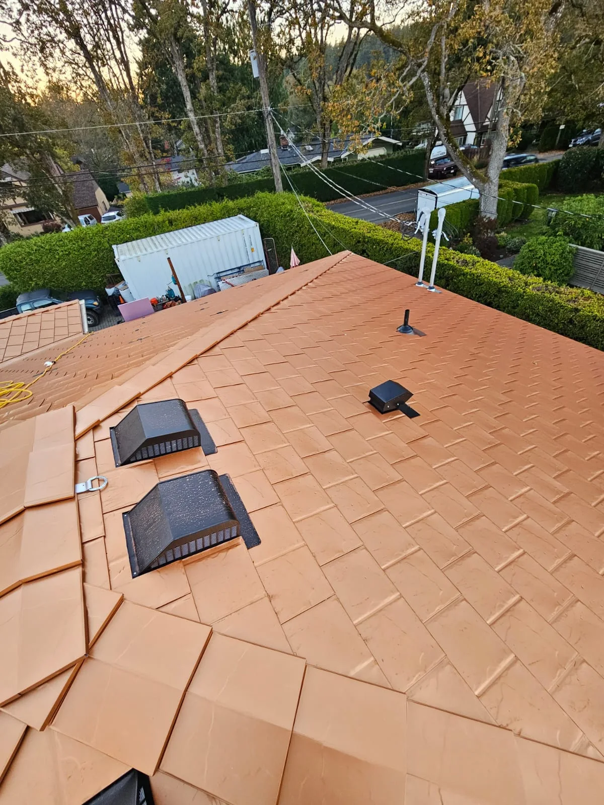 Copper Penny Interlock Slate aluminum roof on a brown one-storey home with a metal roof among tall trees, Victoria, British Columbia