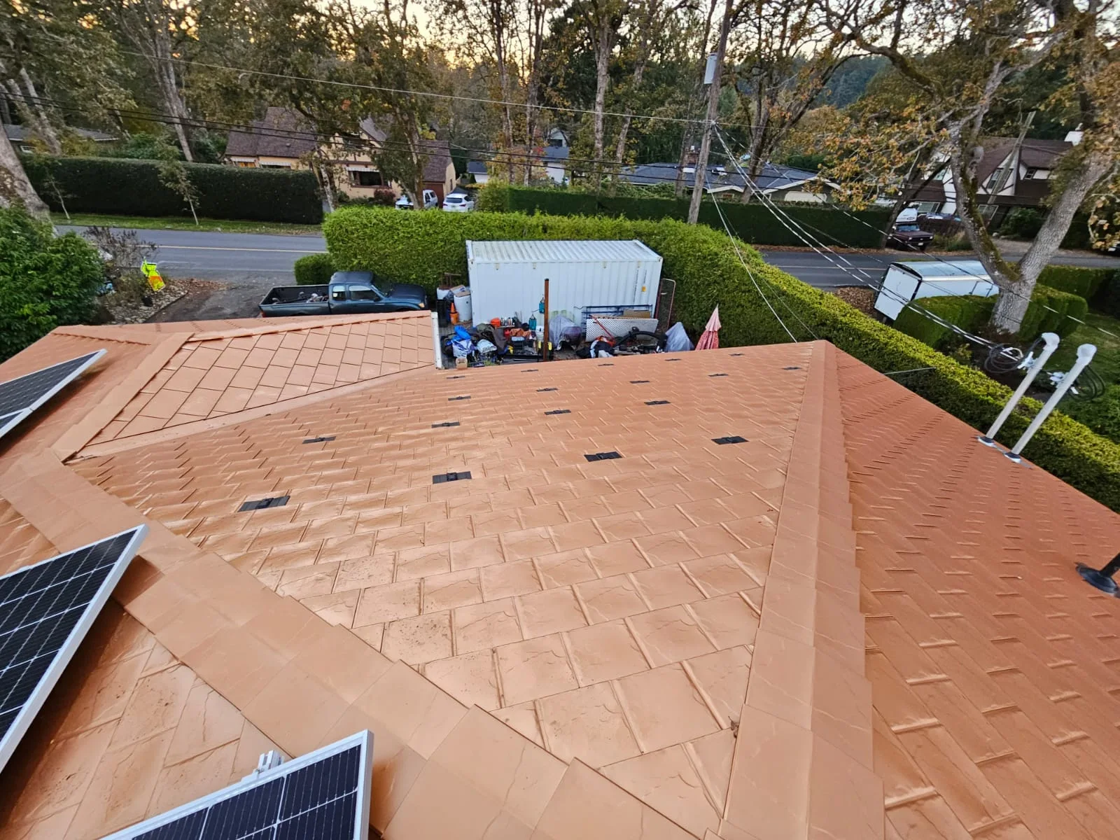 Copper Penny Interlock Slate aluminum roof being installed on a modern home with a metal roof among suburban trees, Victoria, British Columbia