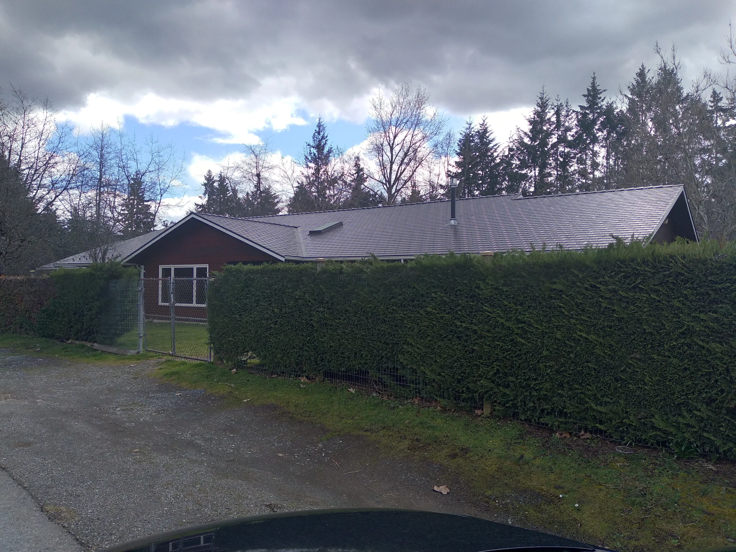 Tudor Brown Interlock Slate aluminum roof on a Tudor brown single-storey home among tall evergreens, Duncan, British Columbia
