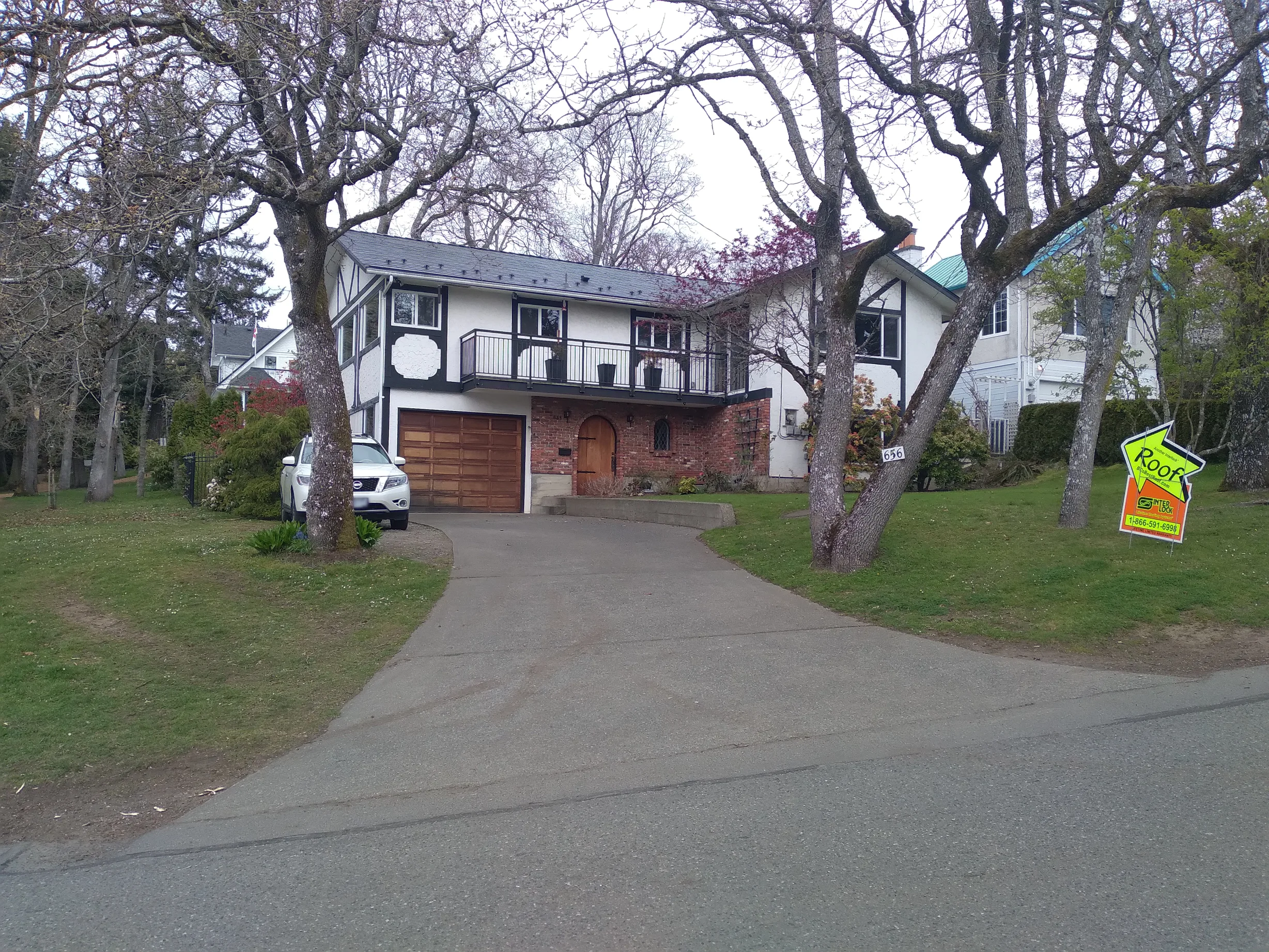 Black Interlock Slate aluminum roof on a white two-storey home with metal roof among tall trees, Victoria, British Columbia