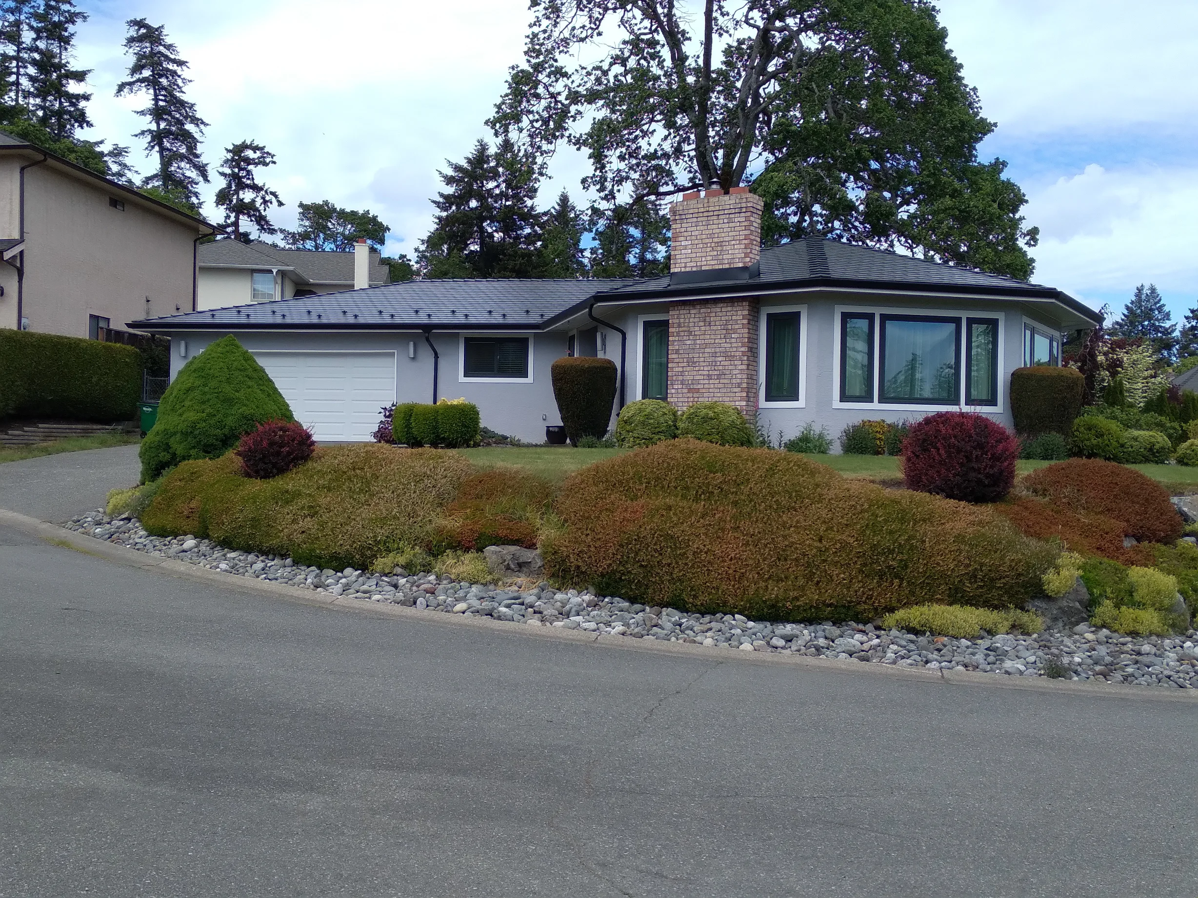 Black Interlock Slate aluminum roof on a two-storey home with dormers among tall trees and lush, Victoria, British Columbia