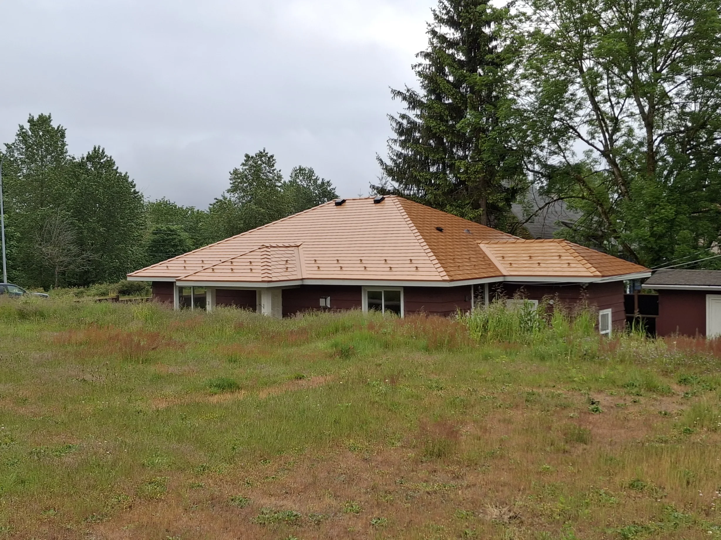 Copper Penny Interlock Slate aluminum roof on a red home with a copper penny metal roof among tall pines, Ladysmith, British Columbia