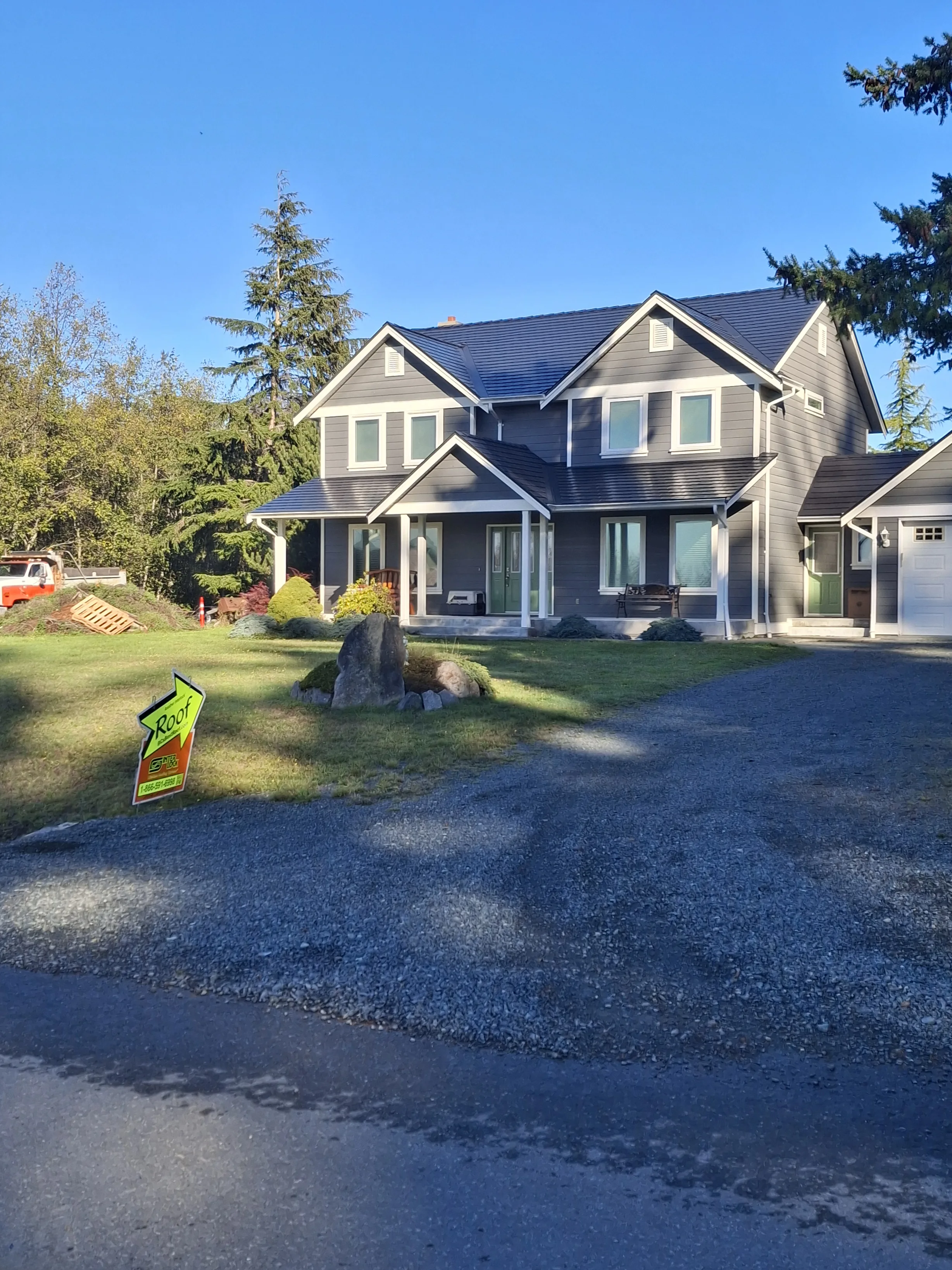 Black Interlock Slate aluminum roof on a two-storey grey home with a metal roof in a forested area, Sooke, British Columbia