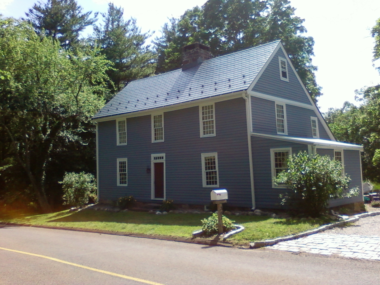 Two-story Colonial home in Northford, CT clad in blue-grey siding with a steep charcoal grey Interlock aluminum slate metal roof and brick chimney.