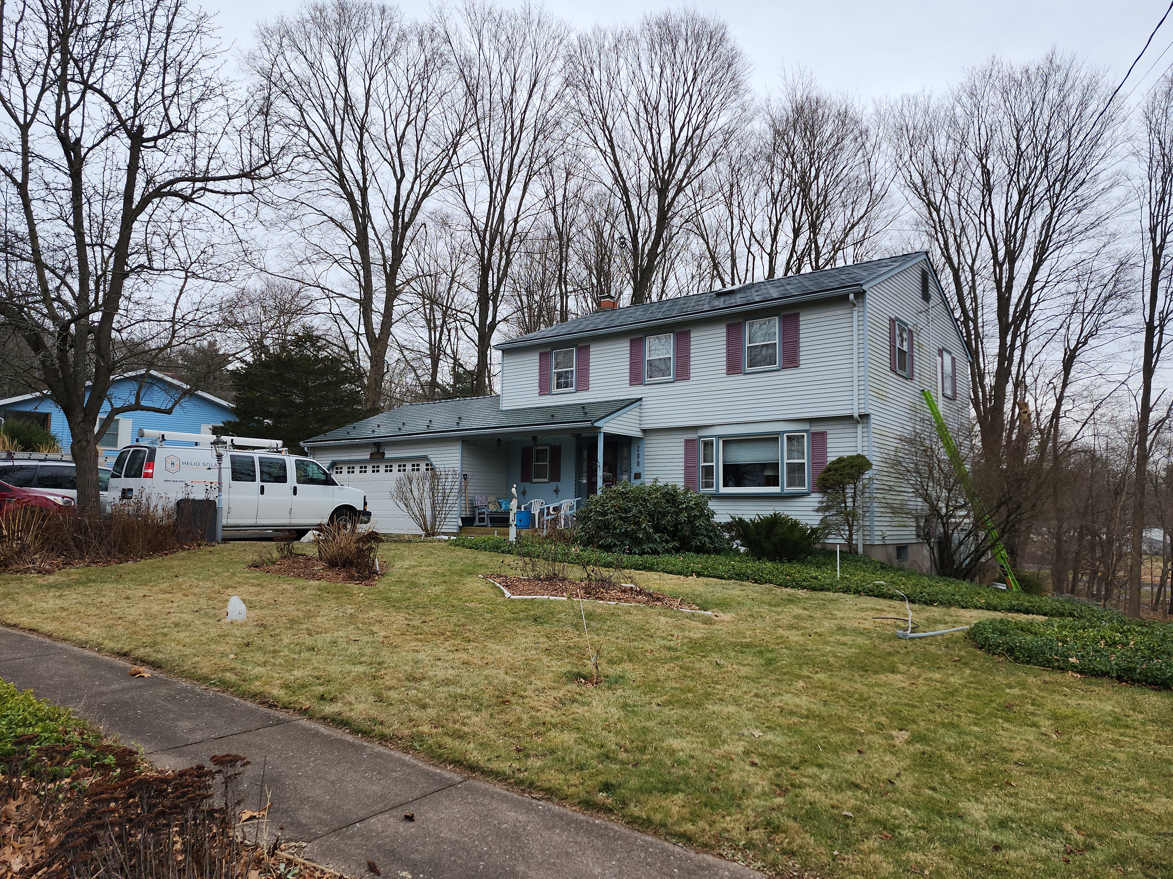 Two-story Colonial home in Manchester, CT with hunter green Interlock aluminum slate metal roof, purple shutters, and chimney, set among bare winter trees.