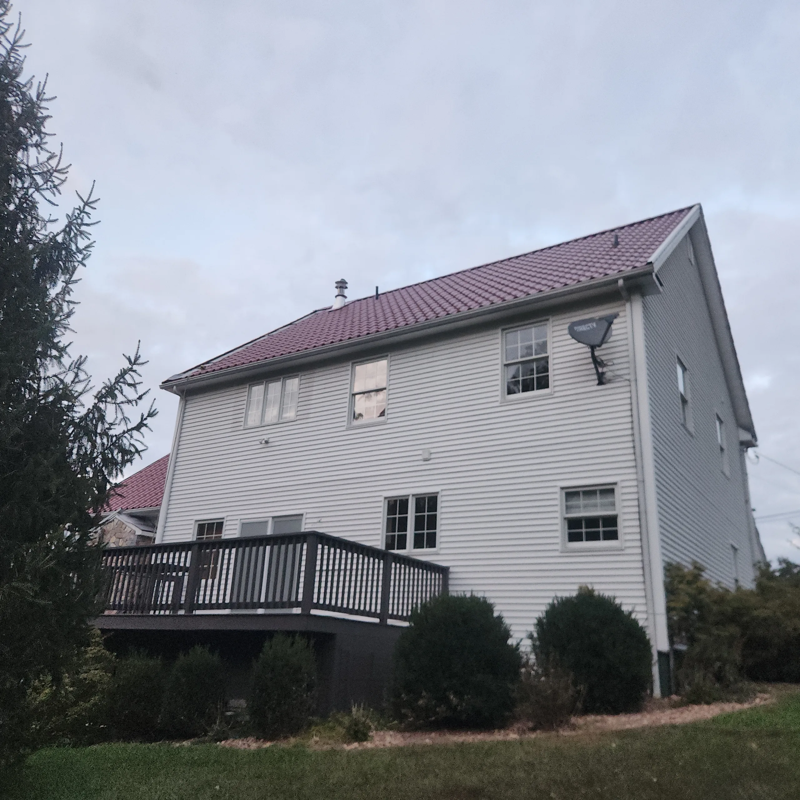 Rear-left view of a 2-story Colonial home in Oxford, CT featuring Interlock Tile Red Mediterranean aluminum tile metal roofing with a dark deck.