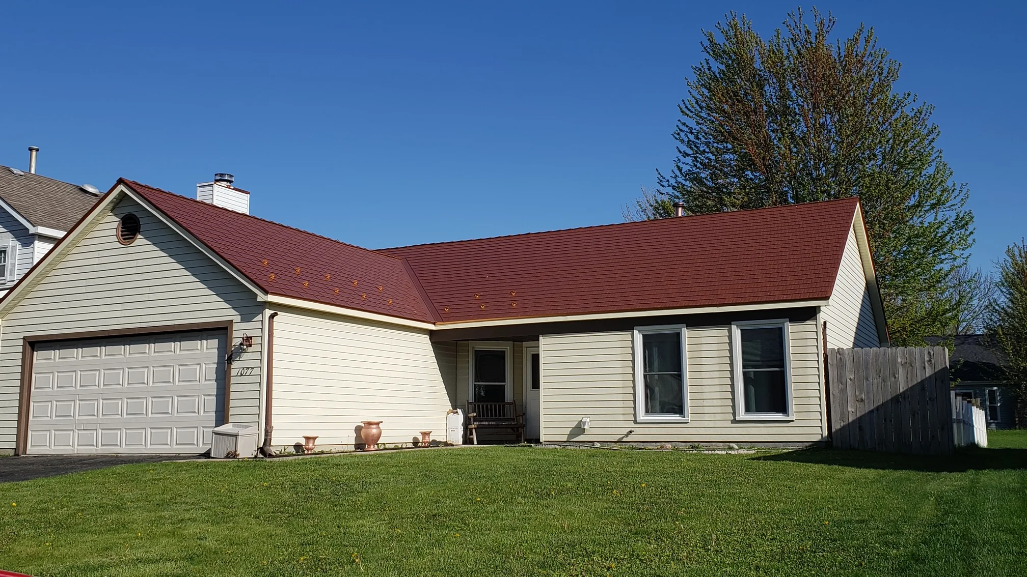 Copper Penny Interlock Cedar Shingle aluminum roof on a cream one-storey home with a metal roof among tall trees, Bolingbrook, Illinois