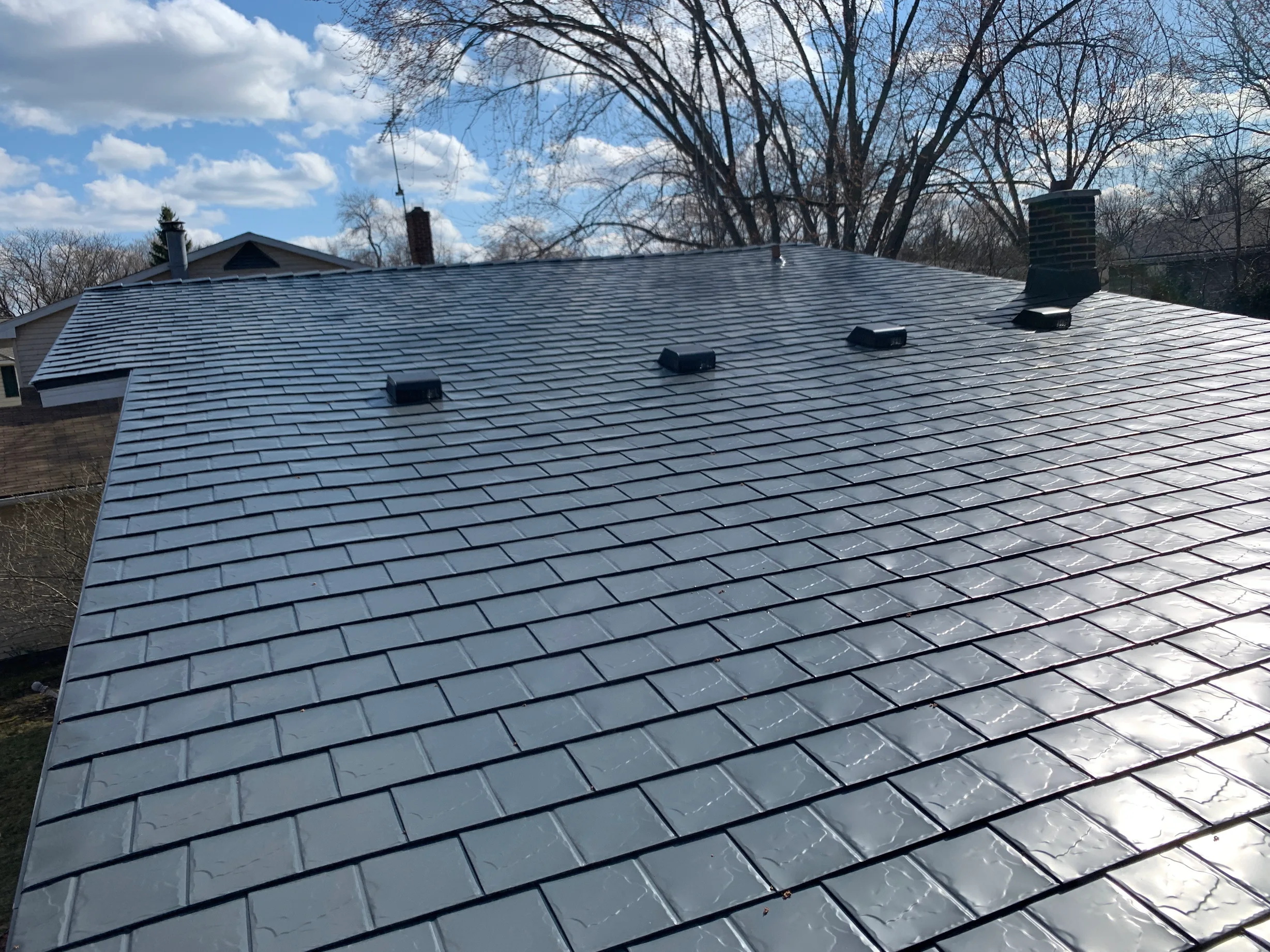 Deep Charcoal Interlock Slate aluminum roof on a single-story home with a metal roof among bare trees, Waukegan, Illinois