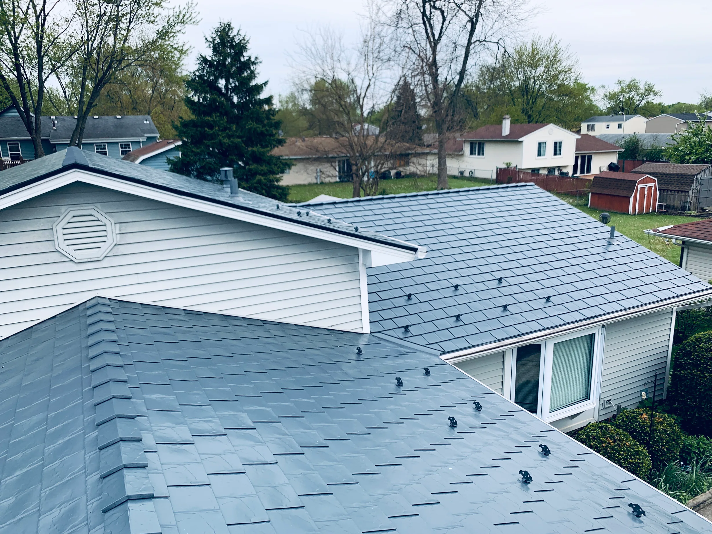 Deep Charcoal Interlock Slate aluminum roof on a white two-storey home with a metal roof among tall trees, Elgin, Illinois
