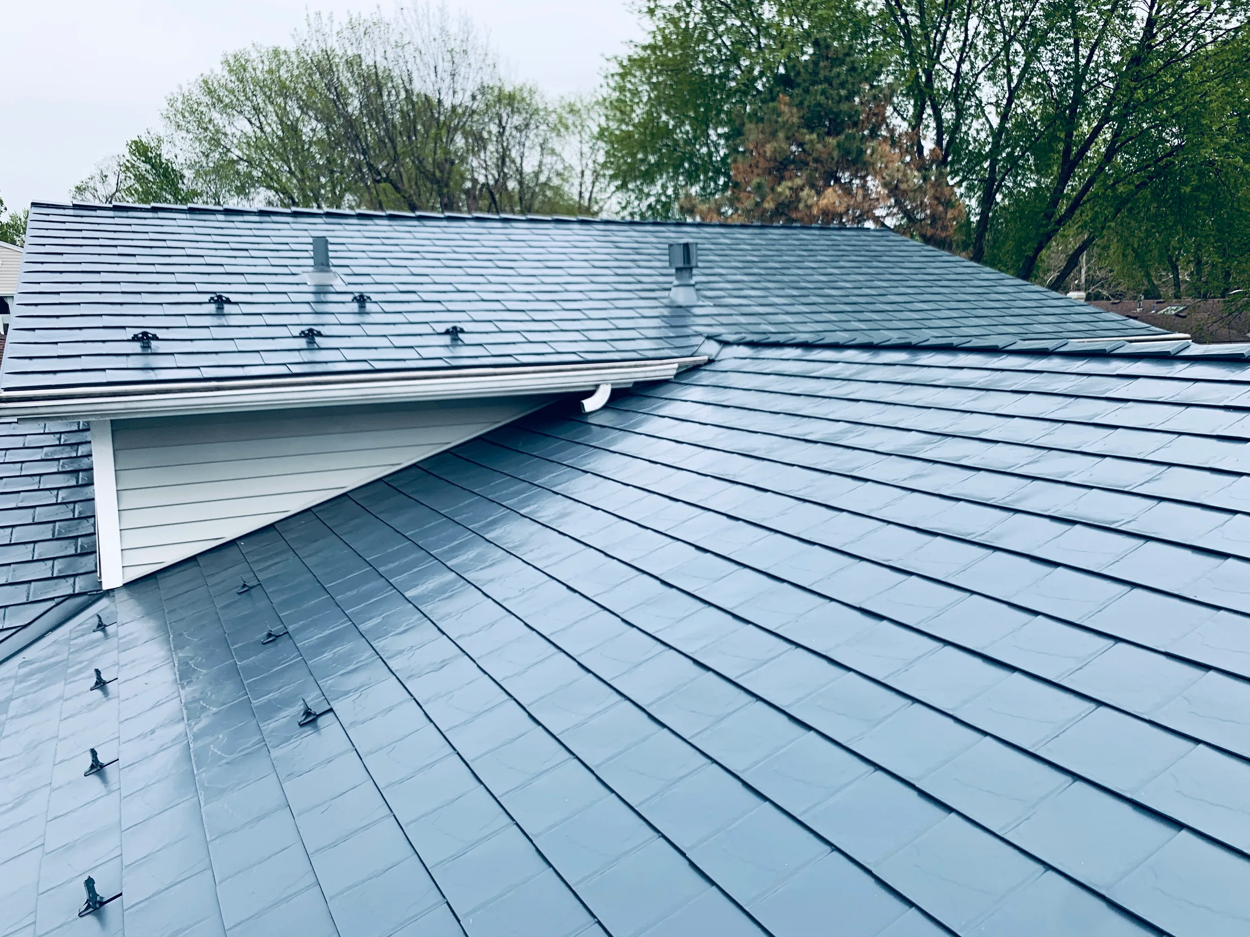 Deep Charcoal Interlock Slate aluminum roof on a grey single-storey home with a metal roof among trees, Elgin, Illinois