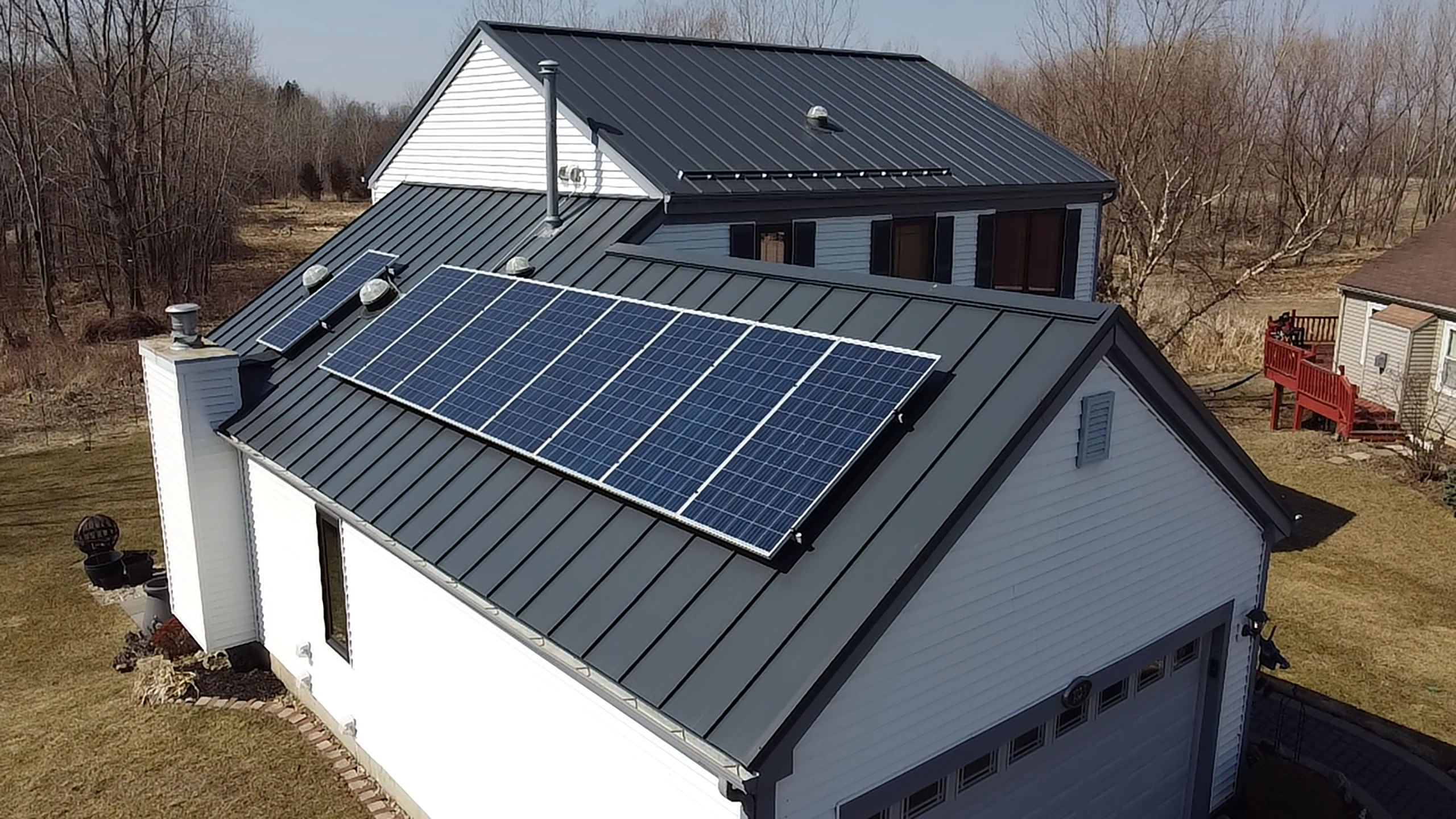 Aerial front view of a farmhouse with Deep Charcoal Interlock standing seam metal roof featuring a large solar panel array and front dormer.